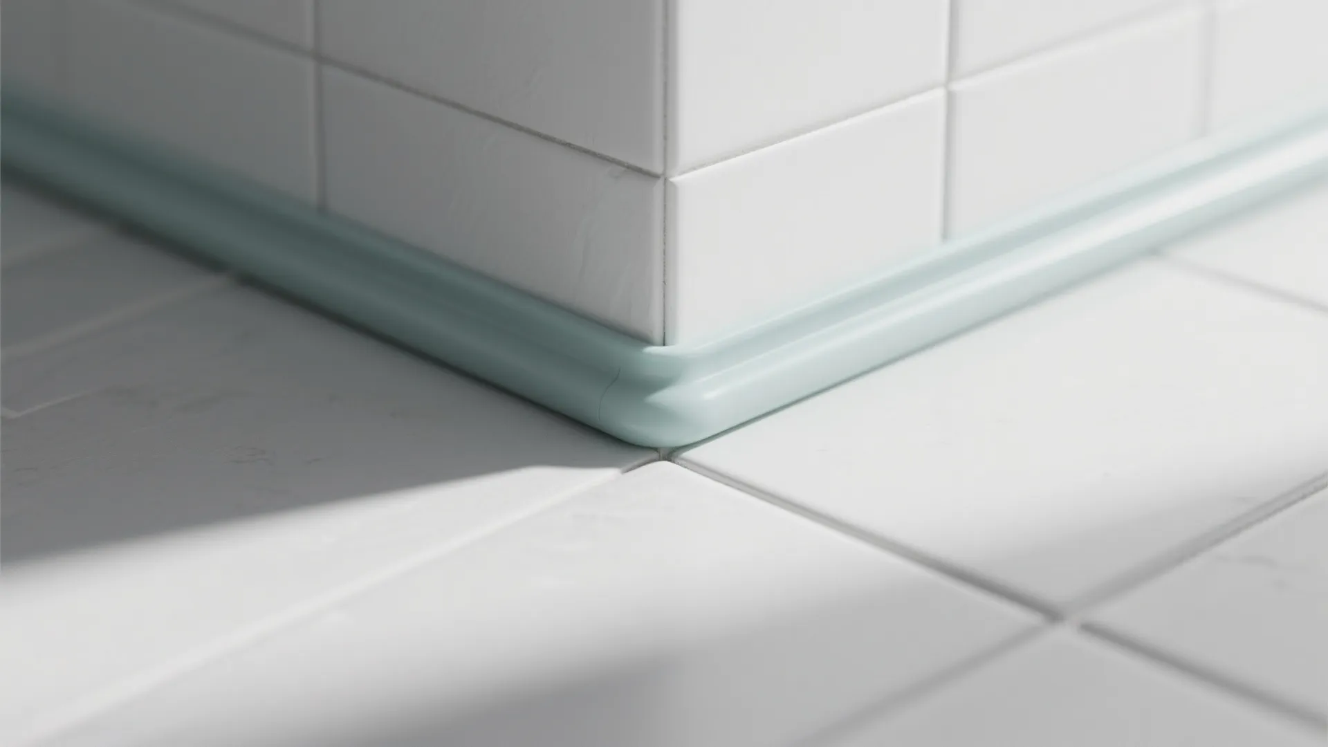 Close up of a bathroom corner showing white wall tiles and light blue waterproof sealant