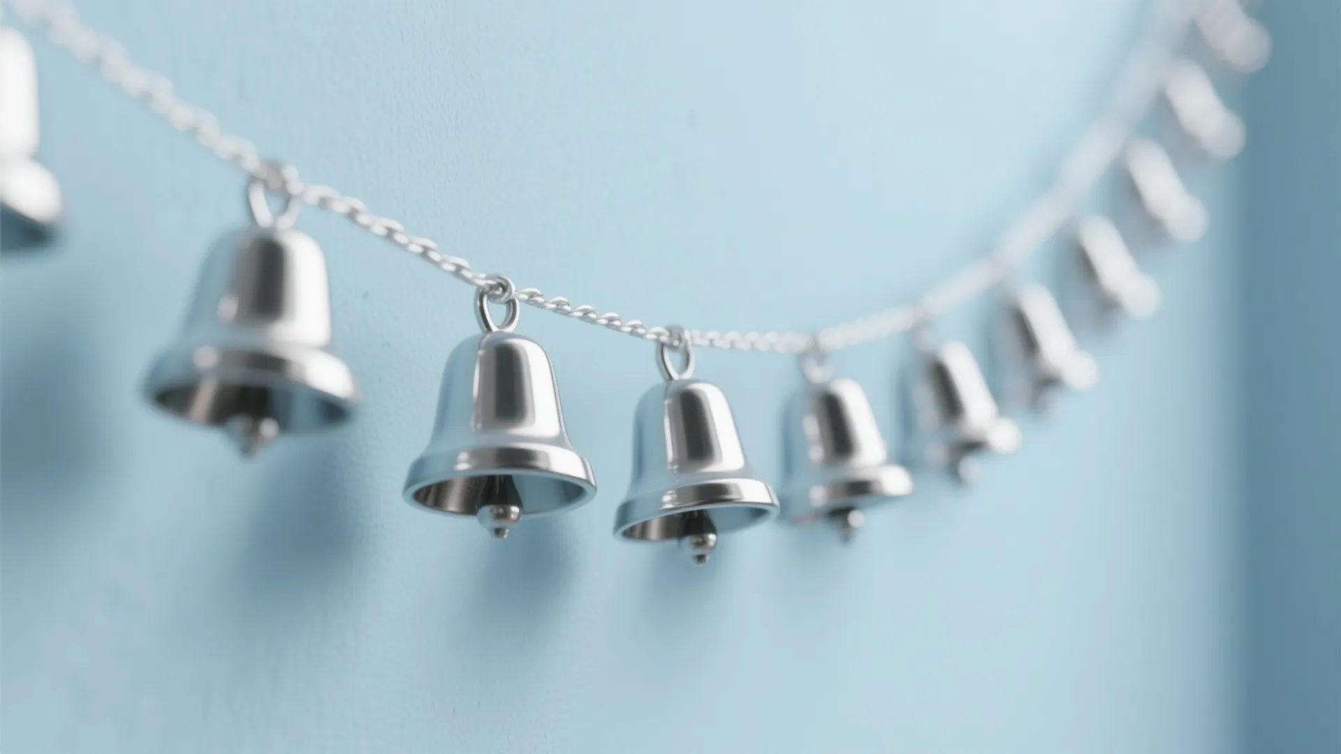 Row of small silver bells hanging on a chain against a light blue wall background