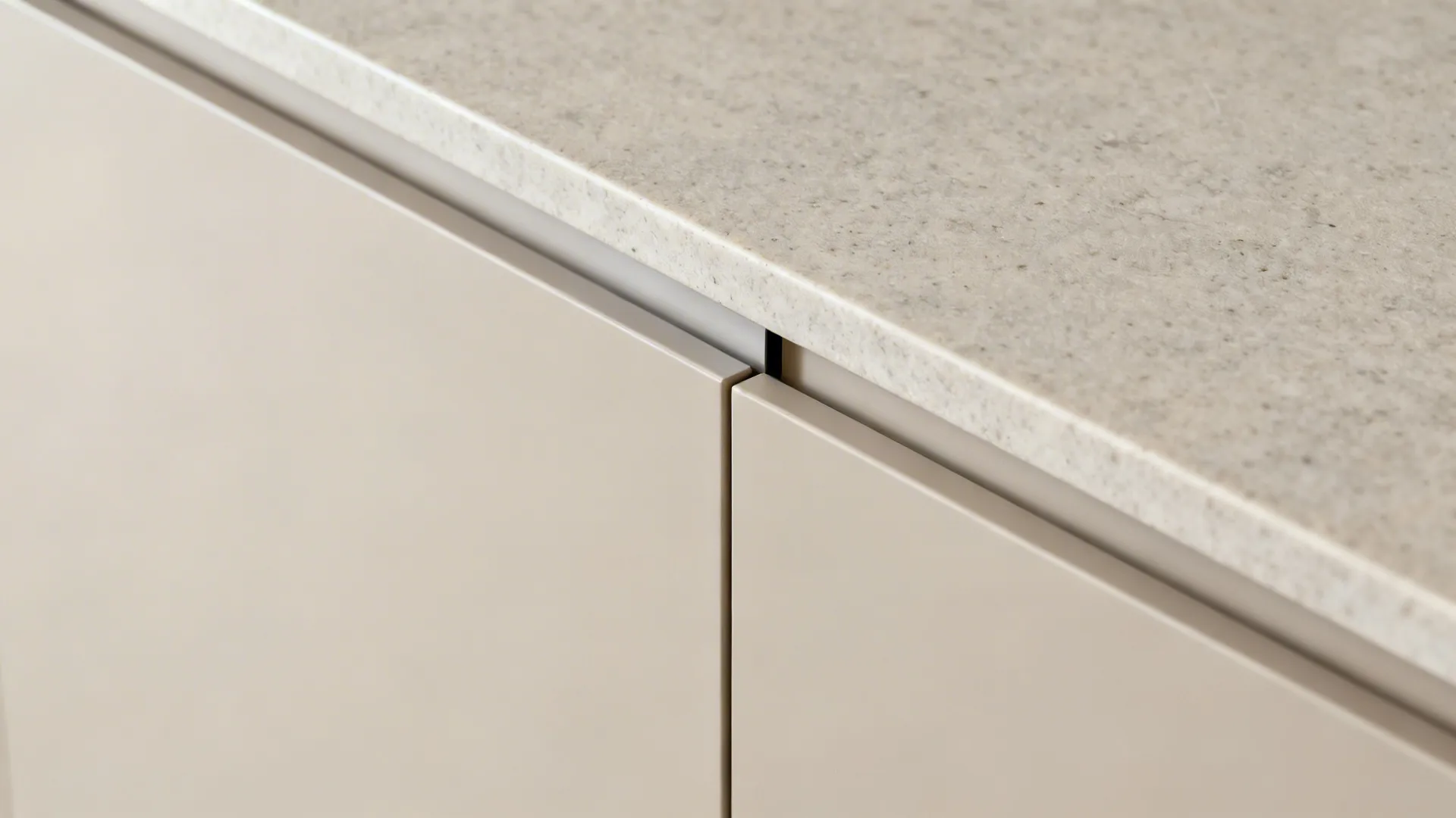 Macro of matte slab cabinet door, slim pull, and stone benchtop junction in soft light.
