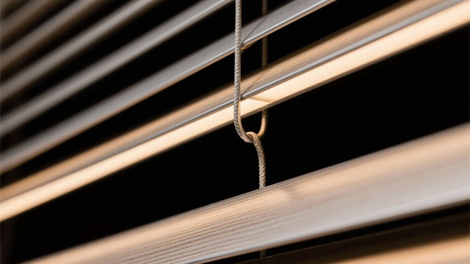 Macro view of light brown wooden window blinds with thin white cord and dark background