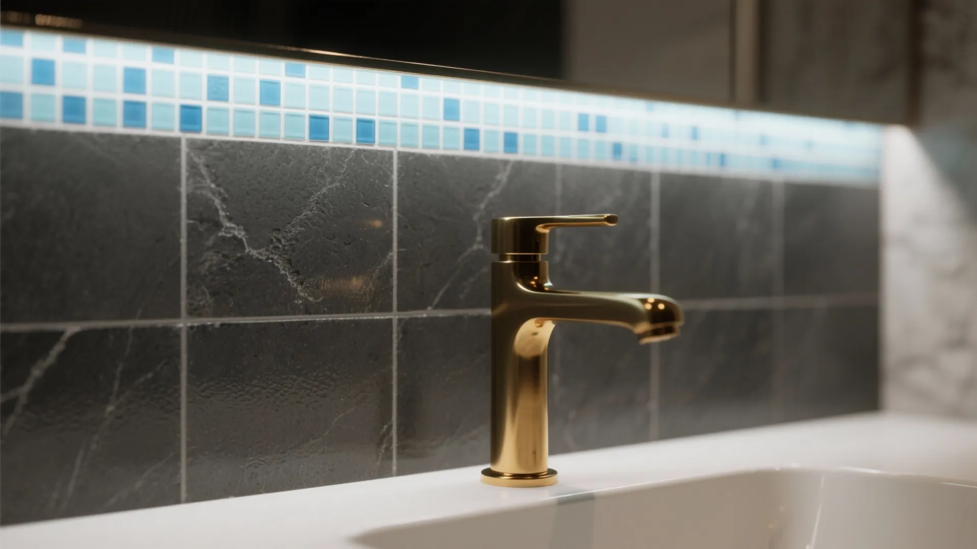 Gold water tap on white bathroom sink with dark grey wall tiles and blue mosaics