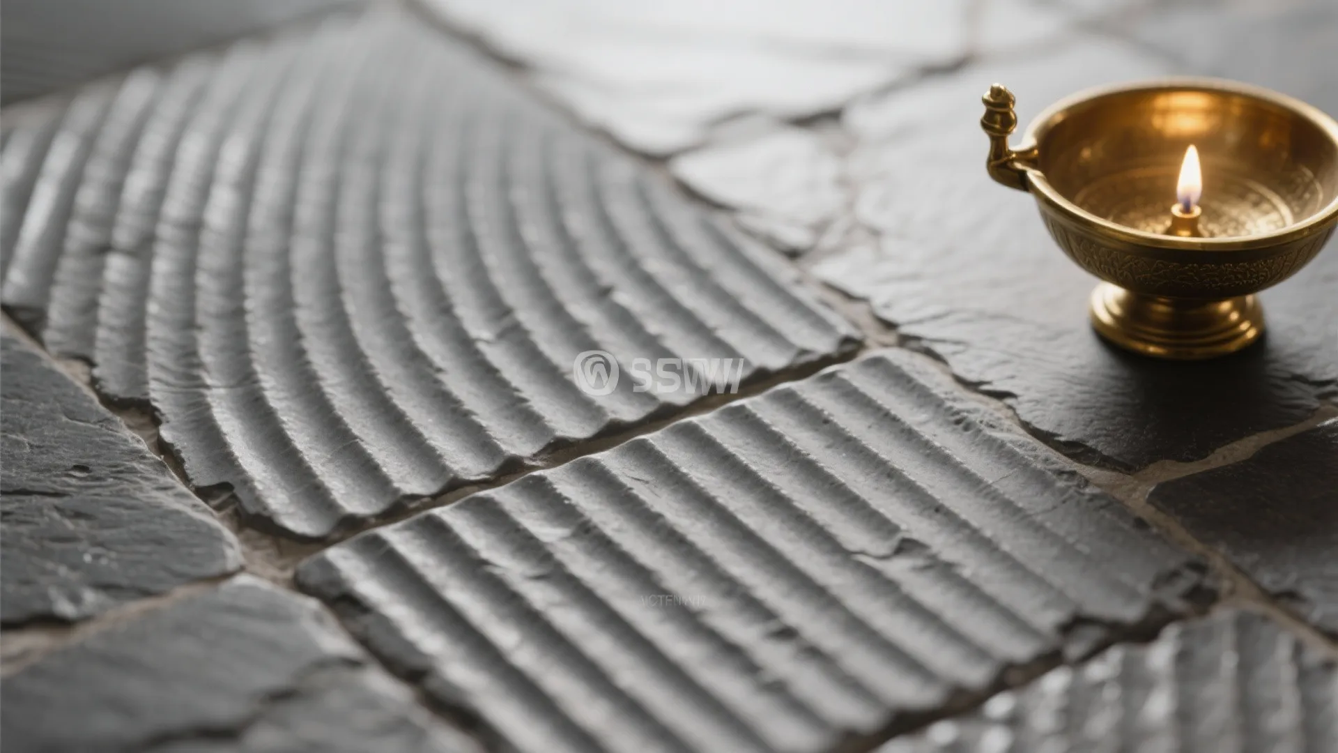 Textured grey stone floor tiles with curved lines next to a small gold metal oil lamp
