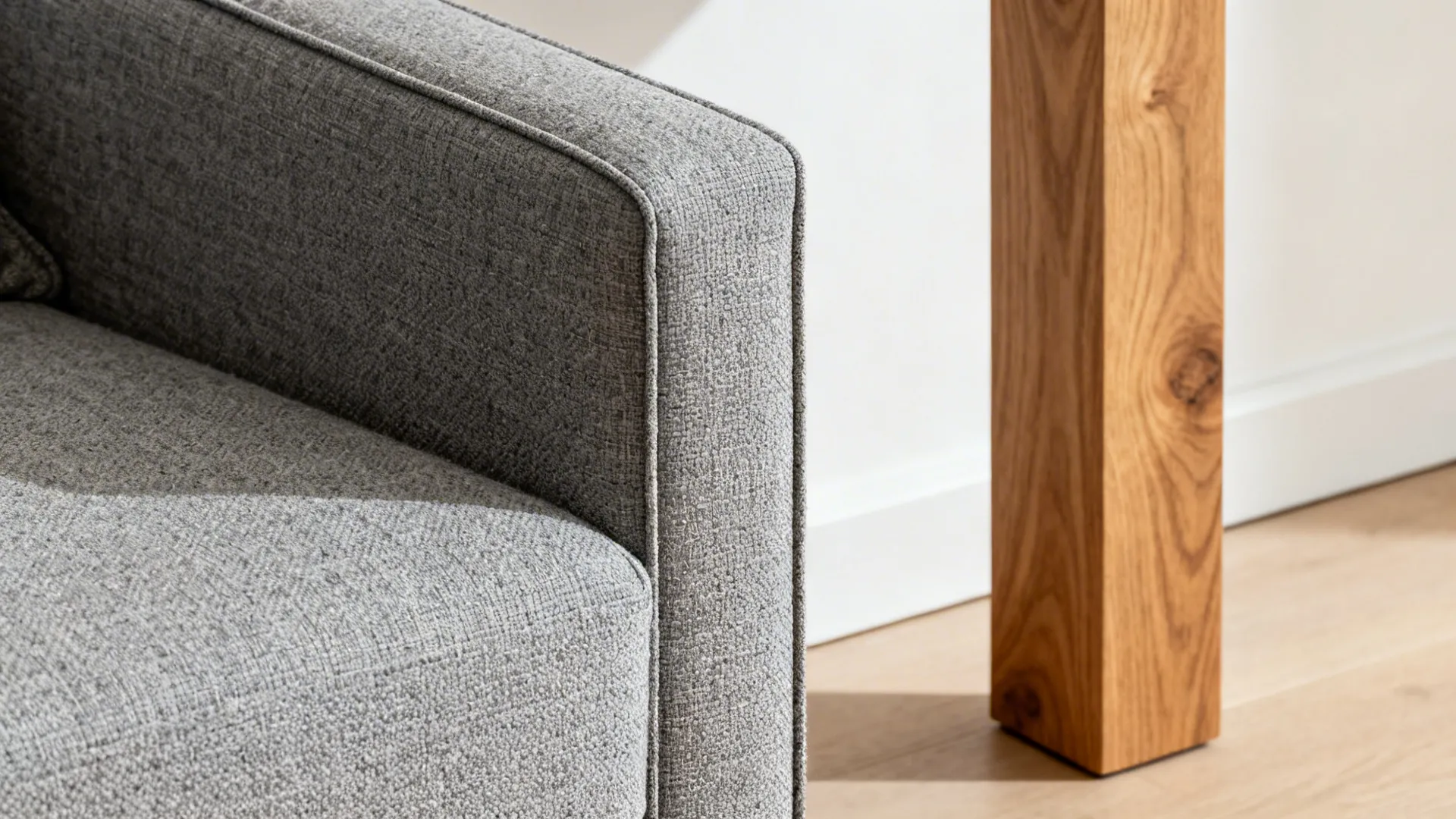 Close-up of a slim sofa arm and tall oak leg with soft daylight.