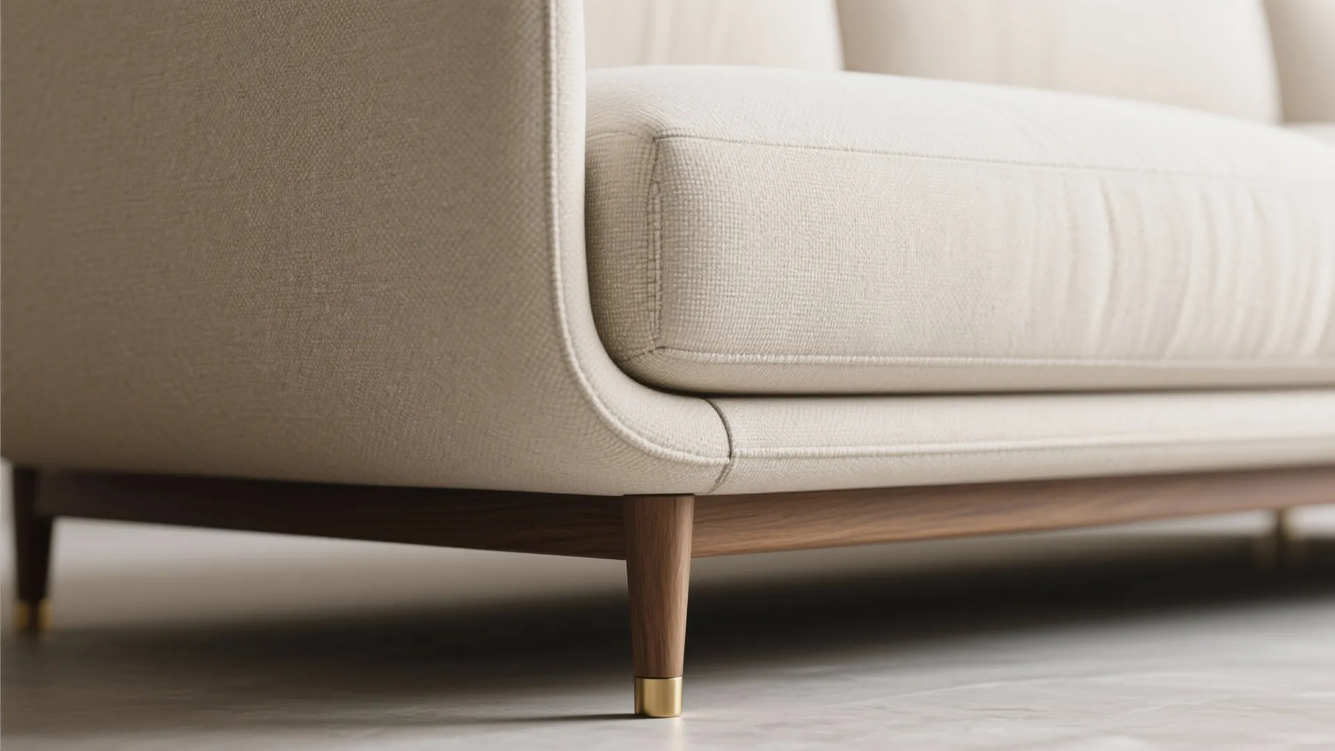 Close-up of a slim curved sectional arm, raised tapered legs and linen texture.