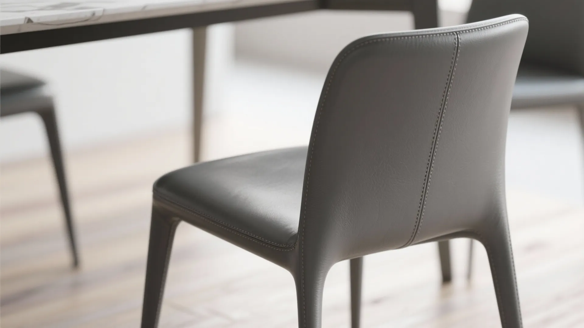 Close up of a grey leather chair with stitching detail next to a dining table