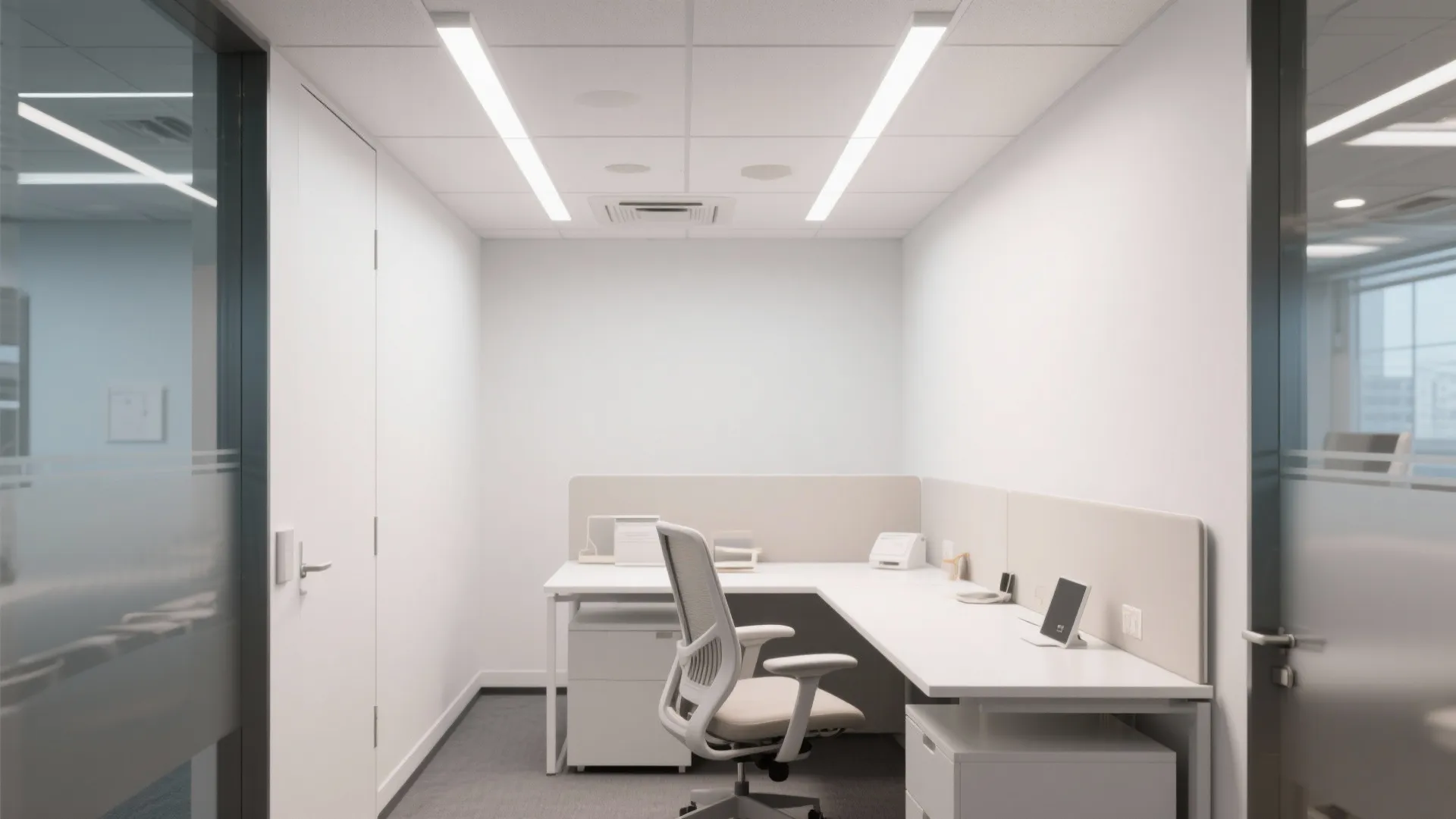 Small white private office space featuring an L-shaped desk and two long ceiling light fixtures