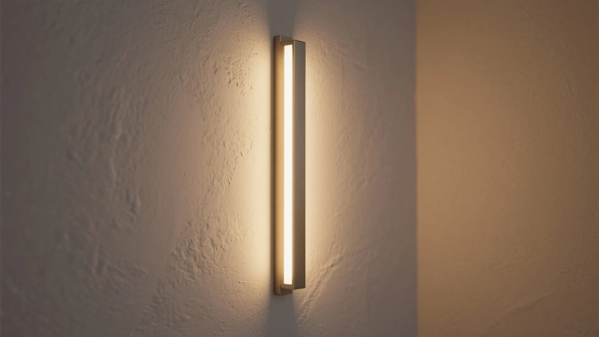 Minimalist vertical wall light glowing with warm yellow light on a textured white plaster wall