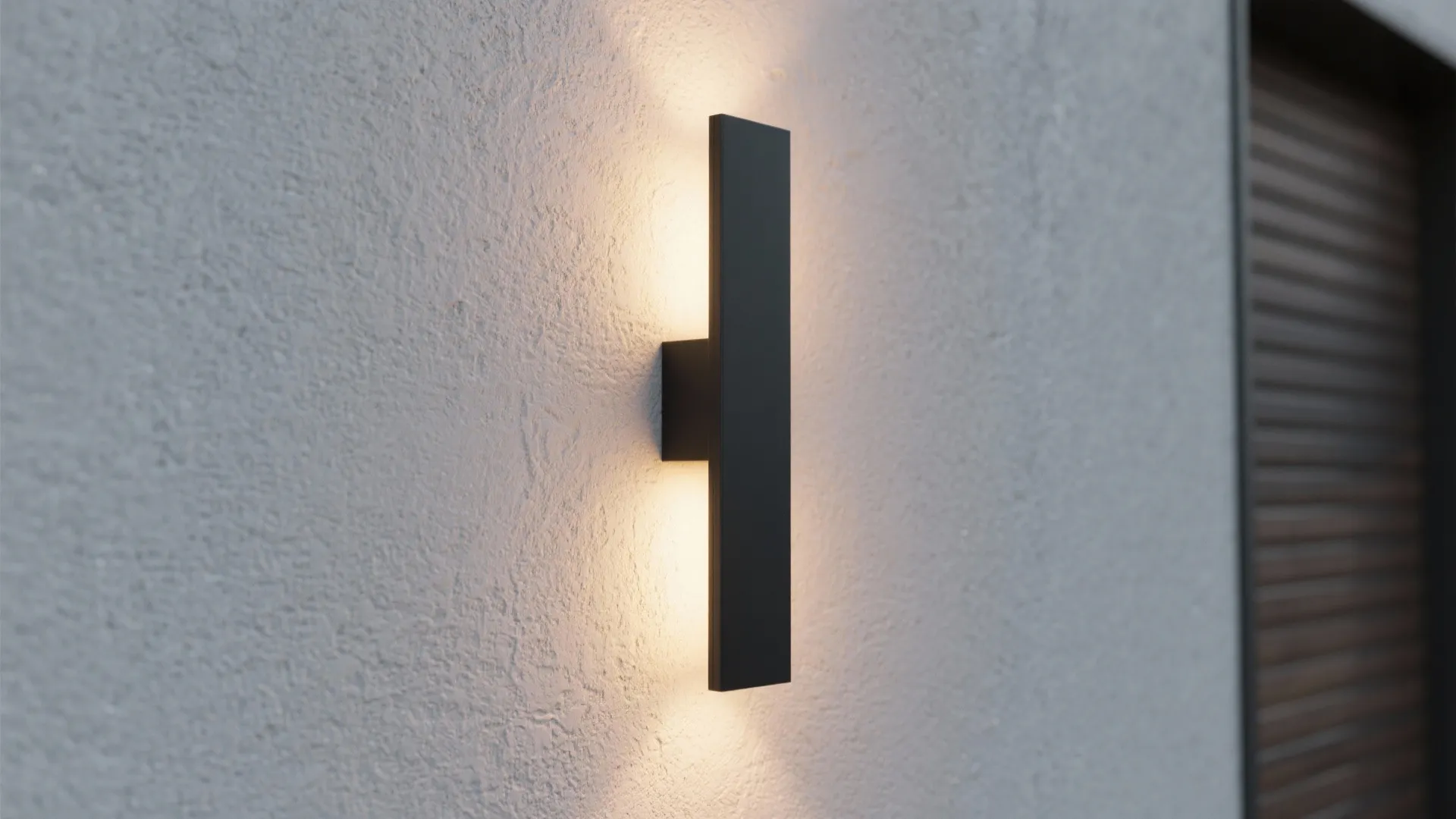 Slim vertical matte-black LED sconce on a textured narrow exterior wall emitting warm wash light.