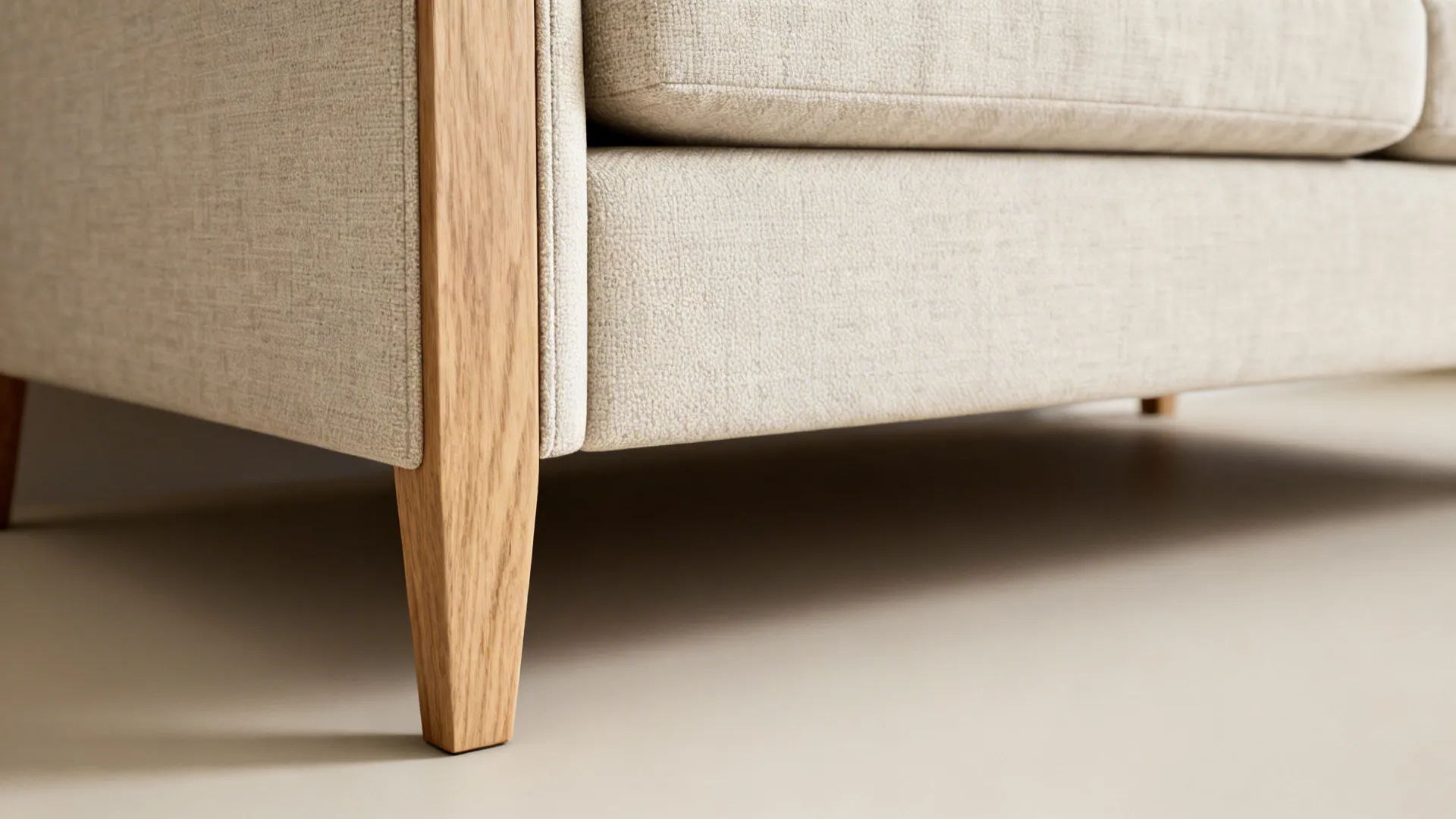 Close-up of a slim loveseat showing narrow arm and exposed wooden leg with textured fabric