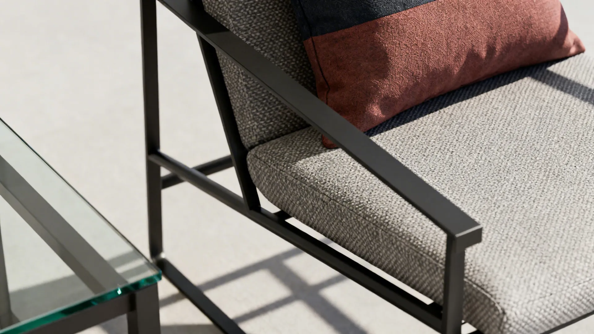 Slim metal-frame lounge chair with lumbar pillow and glass table beside it