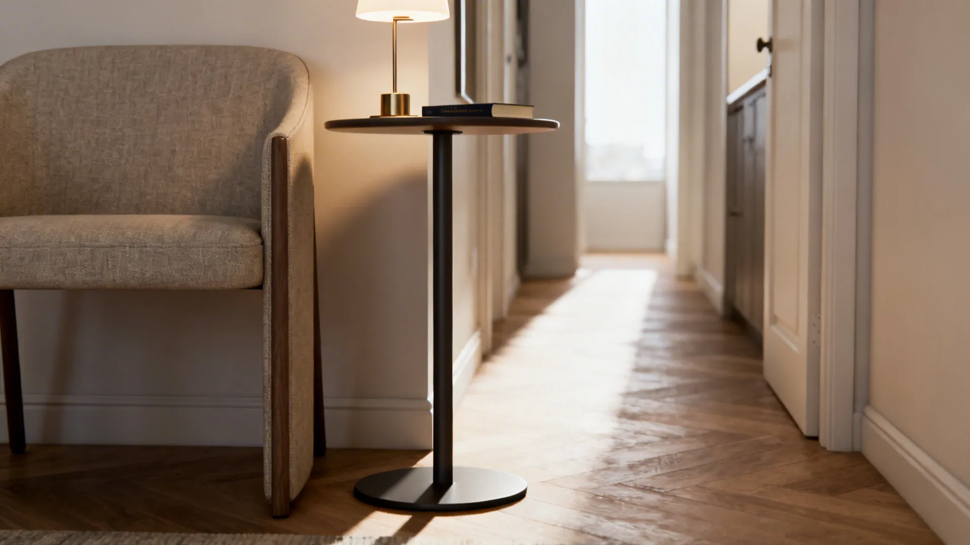 Slim pedestal round table with weighted base beside a narrow armchair holding a lamp and book