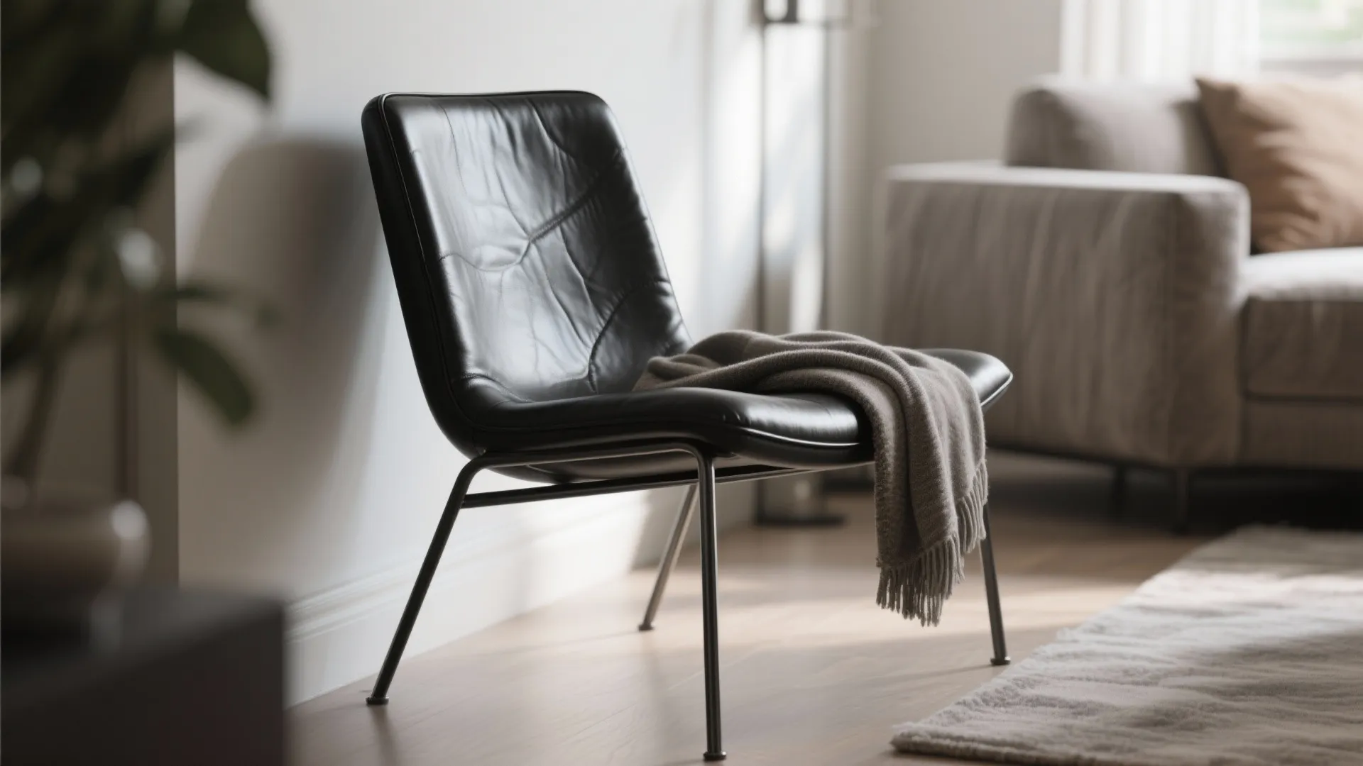 Black leather chair with grey blanket placed on wooden floor next to a white wall