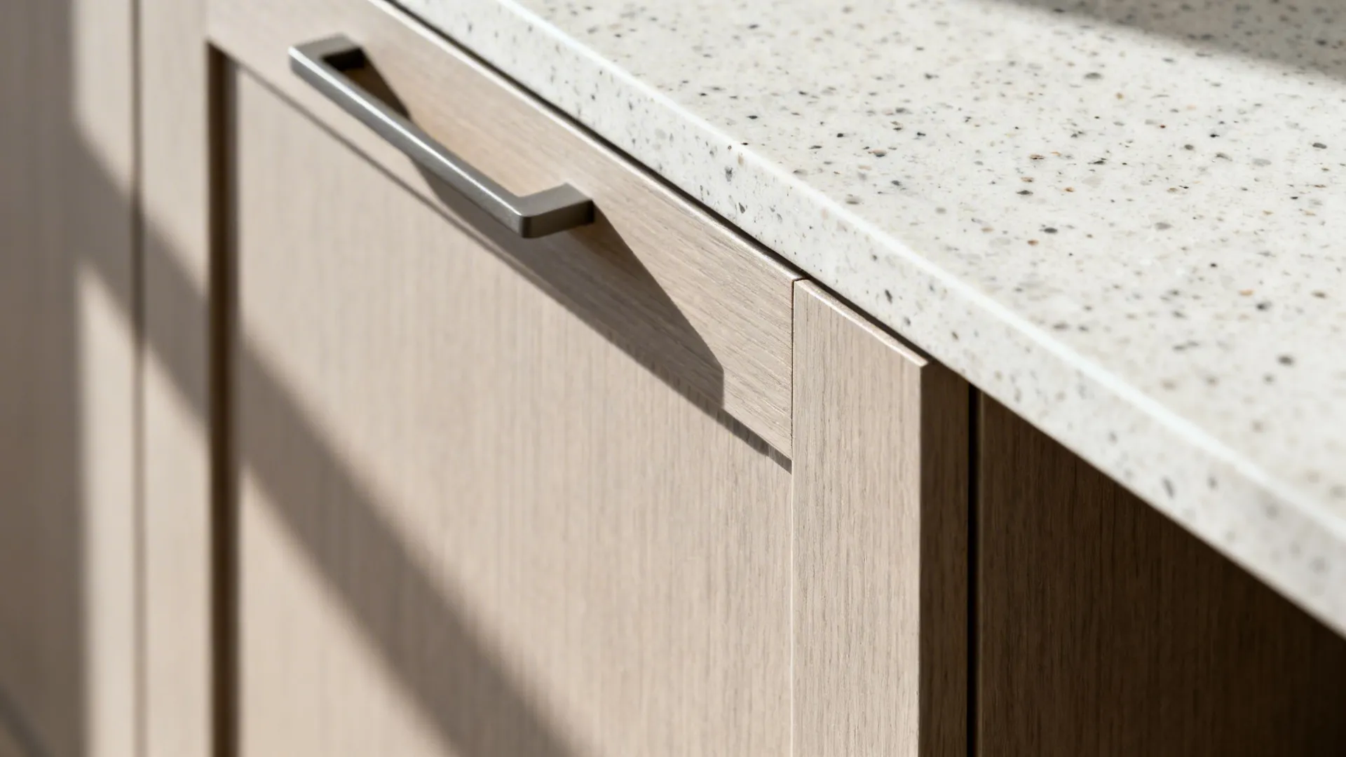 Macro of slim shaker door with integrated pull and matte finish beside light quartz countertop.