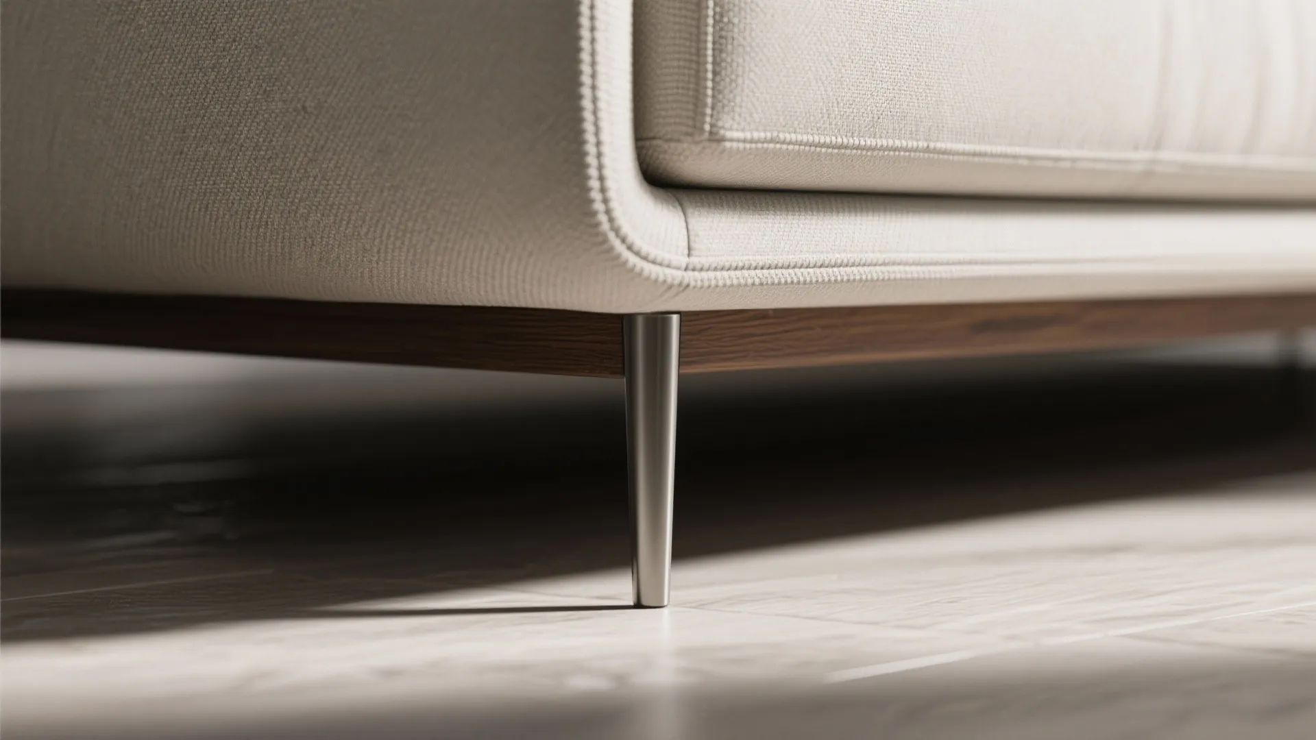 Close up of slim metal sofa legs on wood floor with light beige fabric seat