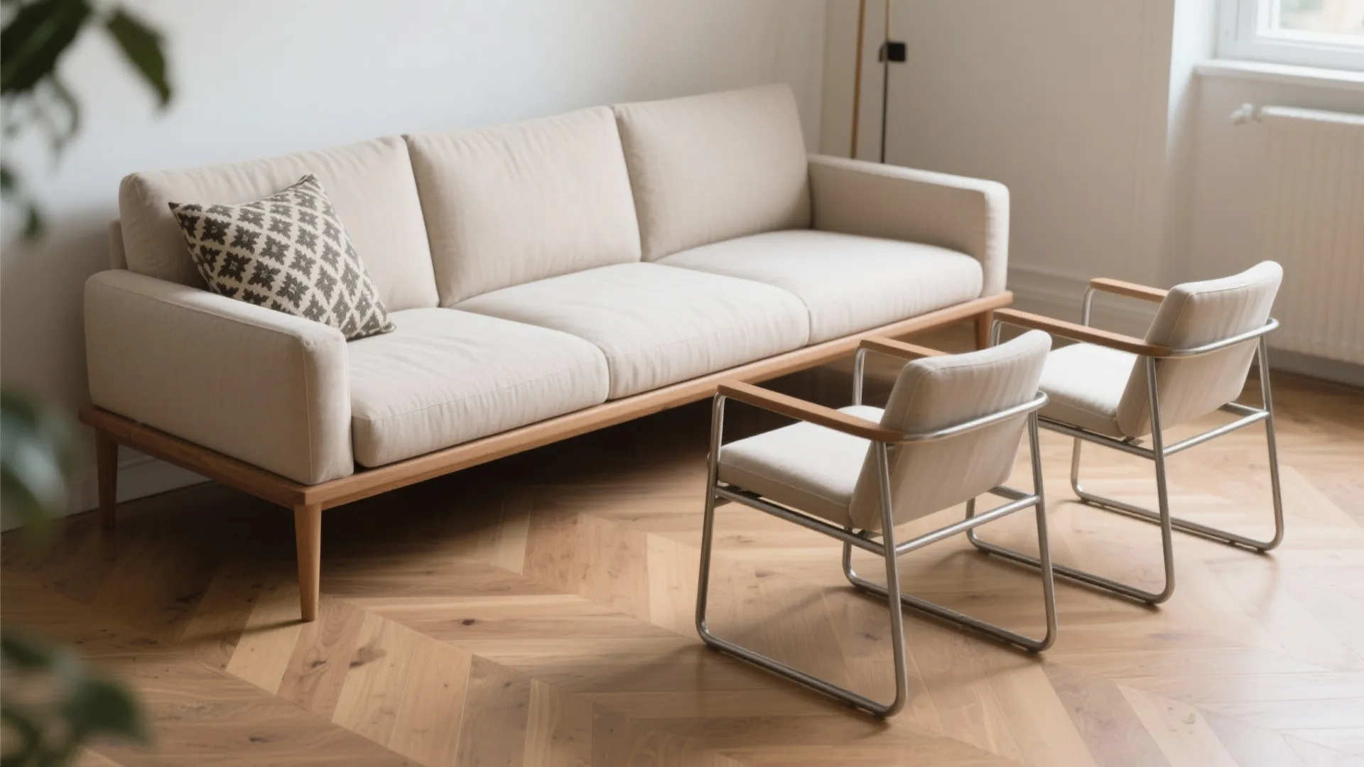 Cream sofa with patterned pillow and two metal frame chairs on a wood herringbone floor