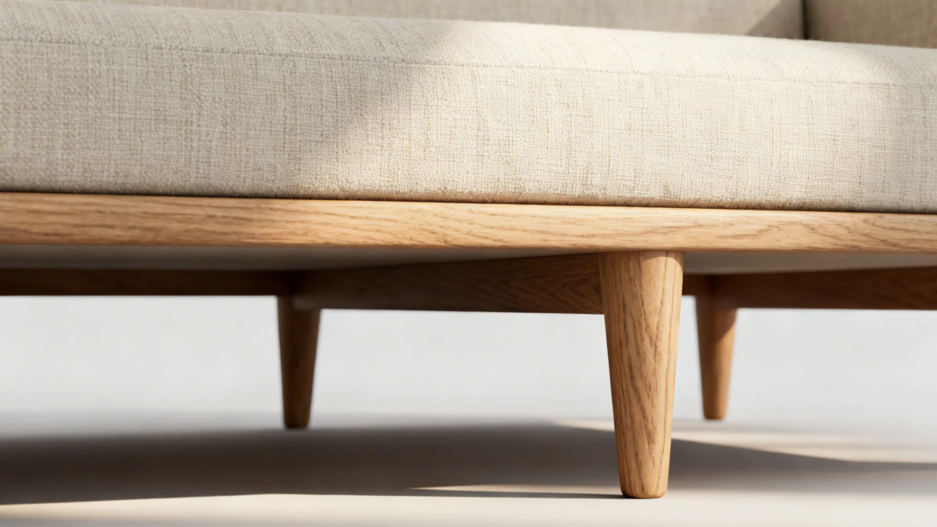 Close-up of a slimline sofa frame with raised wooden legs and visible performance linen texture.