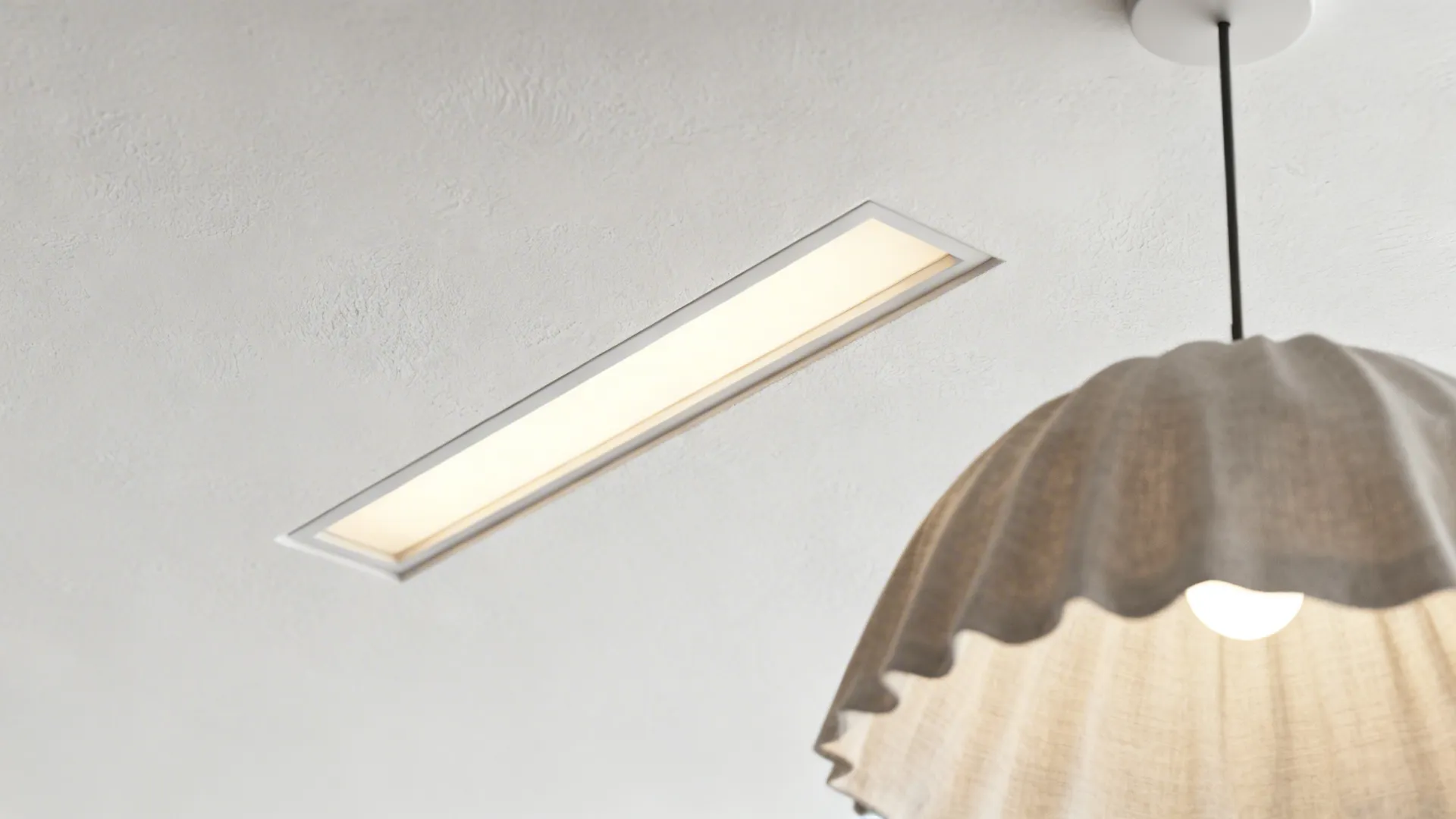 Macro of a trimless recessed light slot near a diffused pendant canopy.