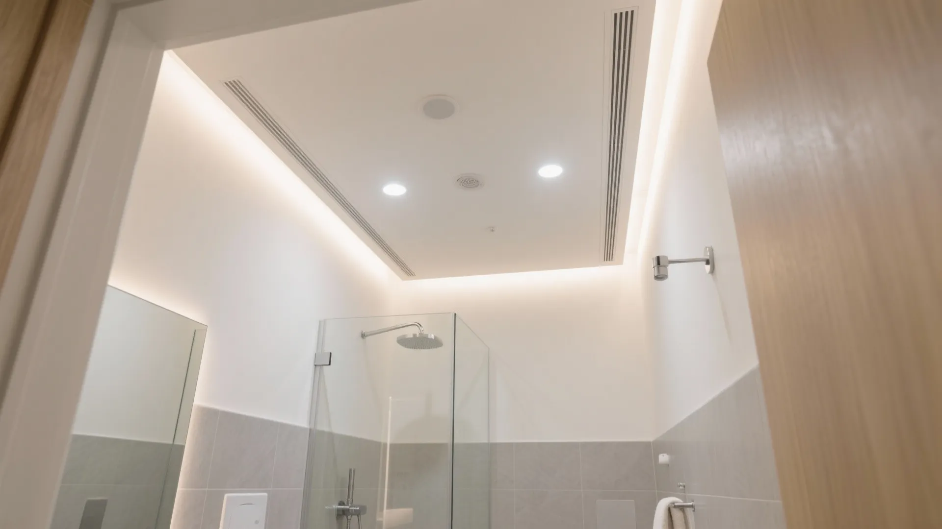 Clean bathroom interior with glass shower screen ceiling light fixtures white walls and grey tiles