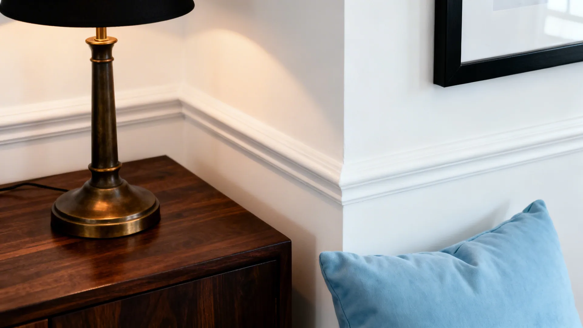 Brass table lamp on dark wood cabinet with white wall panel and a blue pillow