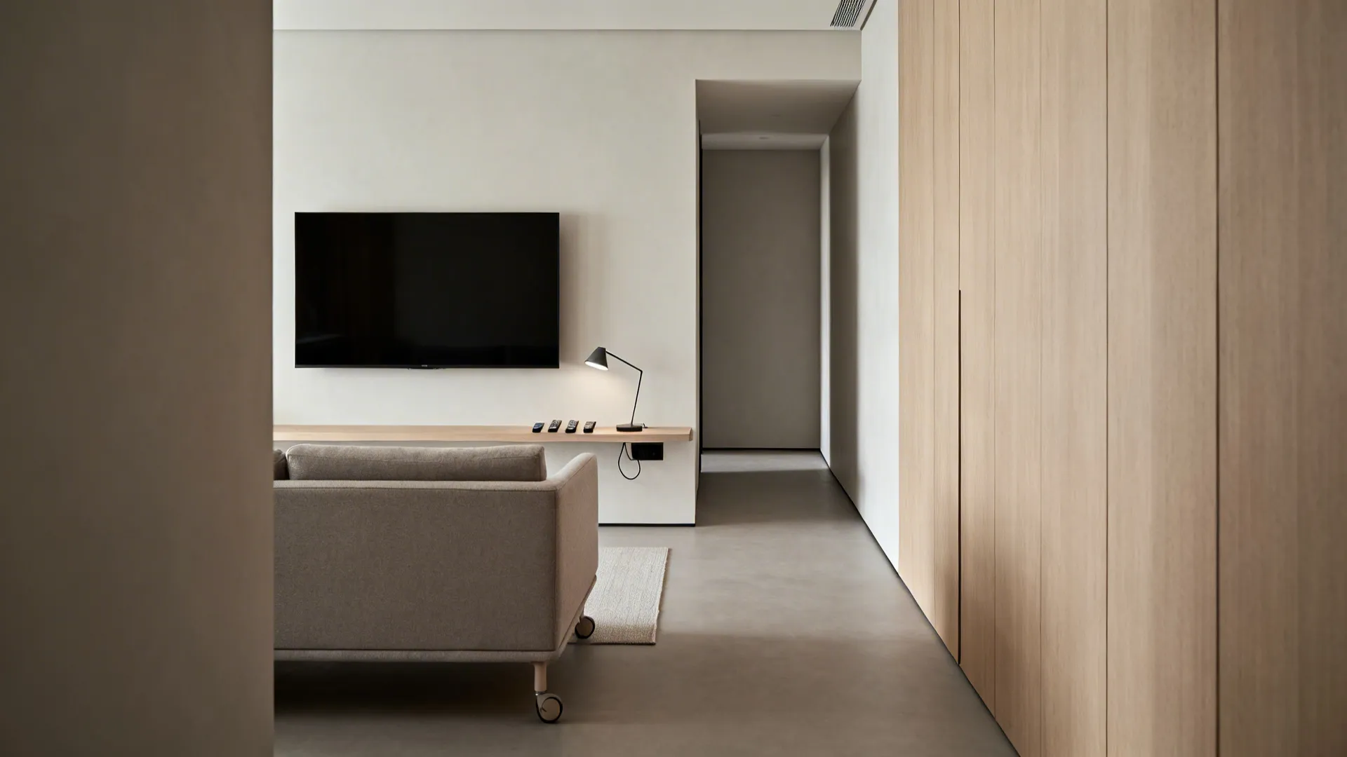 Minimalist living room with grey sofa wooden cabinet wall mounted television and small black desk lamp