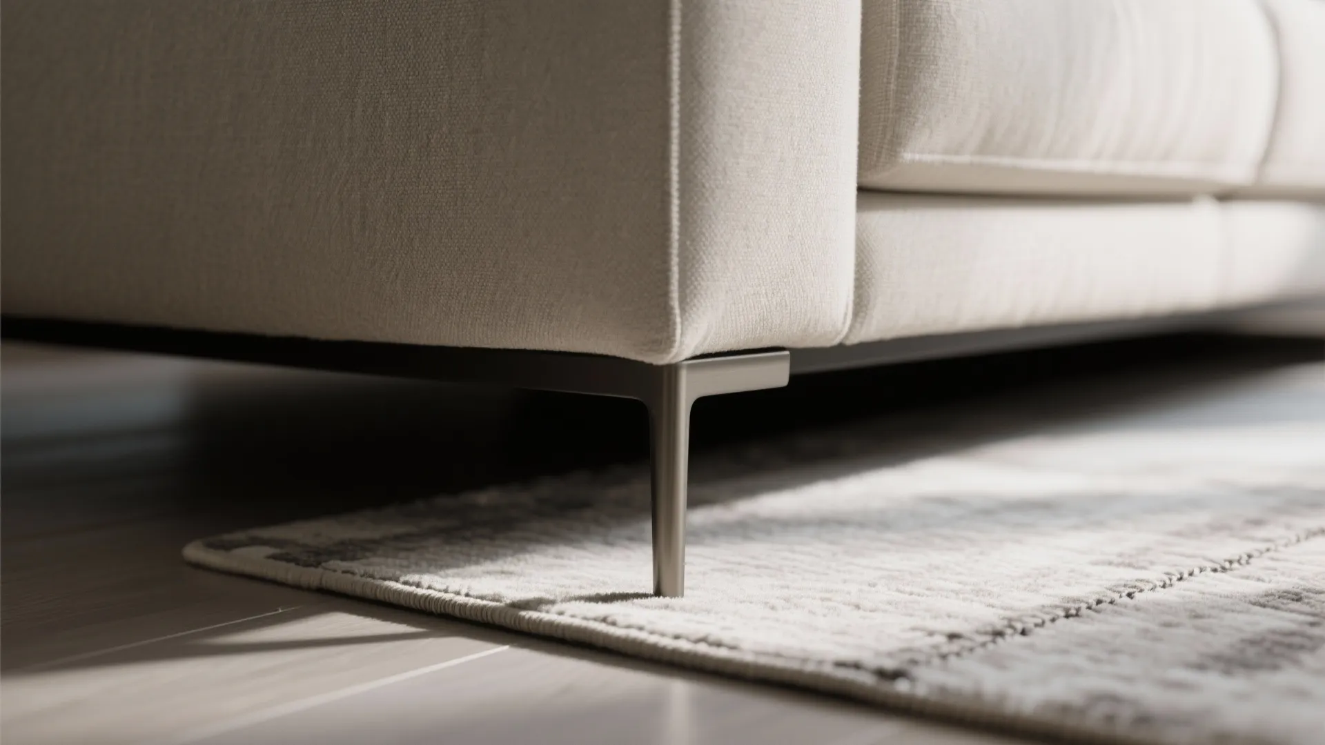Close up view of thin metal sofa leg standing on a grey textured area rug