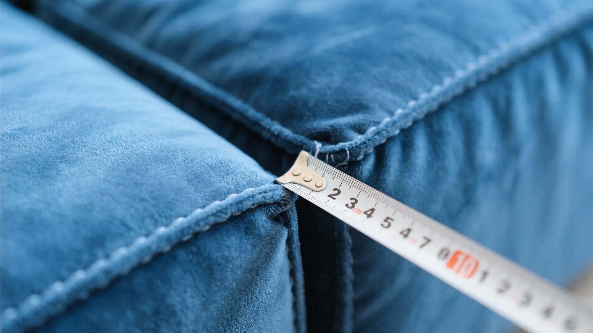 Close up of a metal tape measure checking the size of a blue velvet sofa