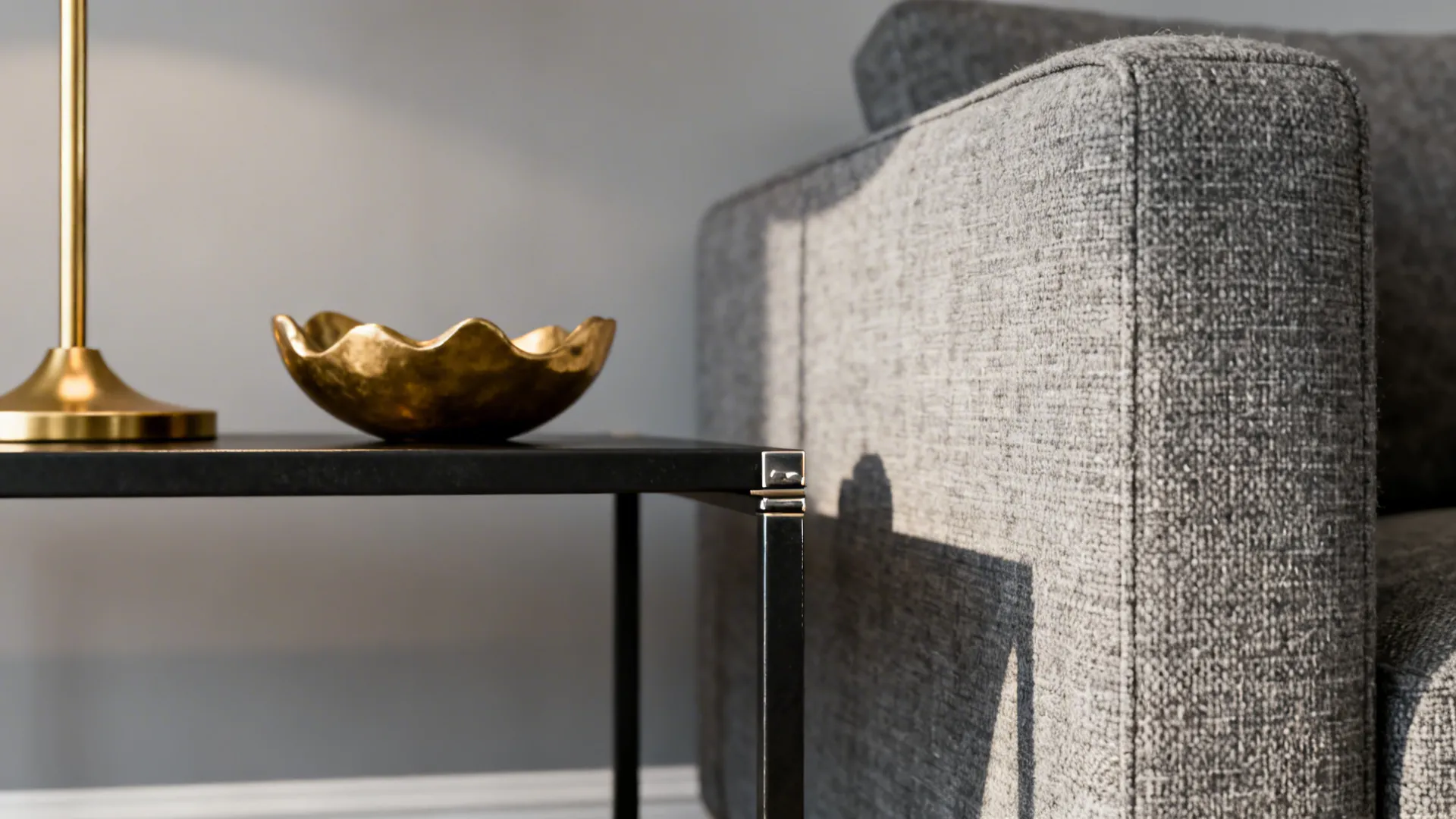 Close-up of grey fabric, black metal table edge and small gold bowl showing texture and finish