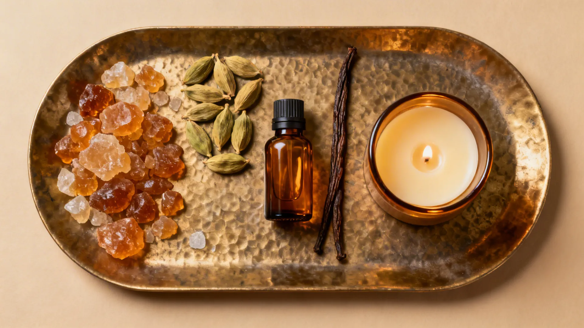 Gold tray with brown glass bottle candle vanilla sticks cardamom seeds and amber stones on table