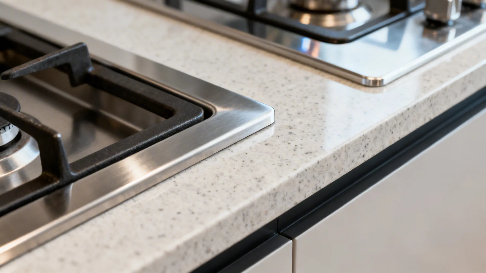Macro of stainless edge trim protecting a quartz countertop cut-out near a gas cooktop.