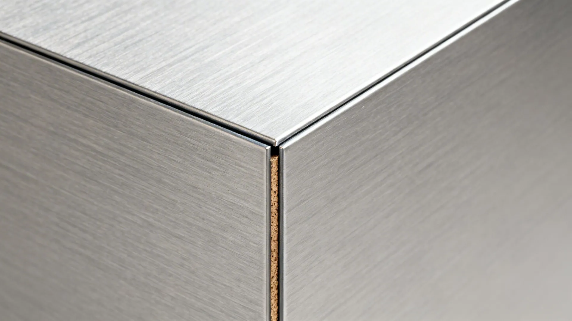 Close up view of a silver brushed metal corner joint on a modern kitchen cabinet surface