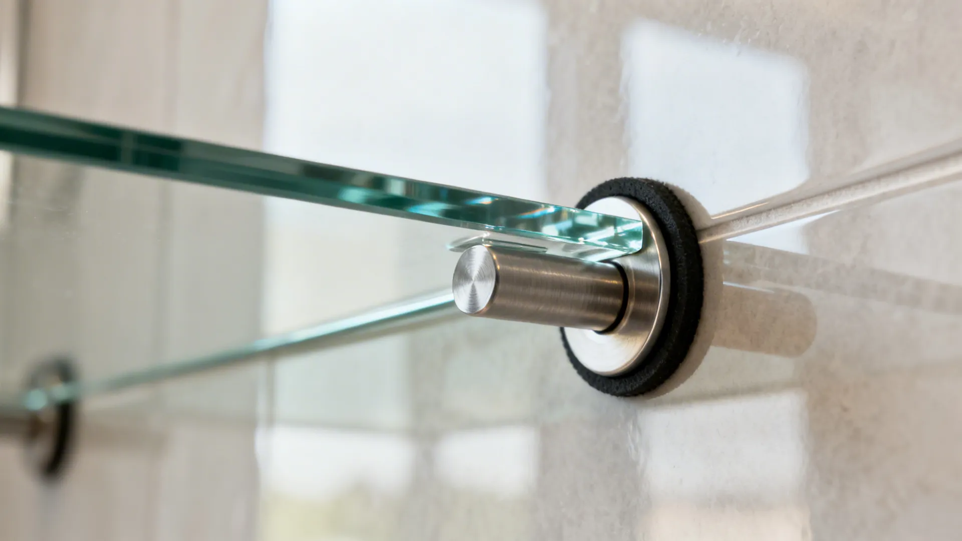 Close up of a metal support piece holding a clear glass shelf against a tiled wall