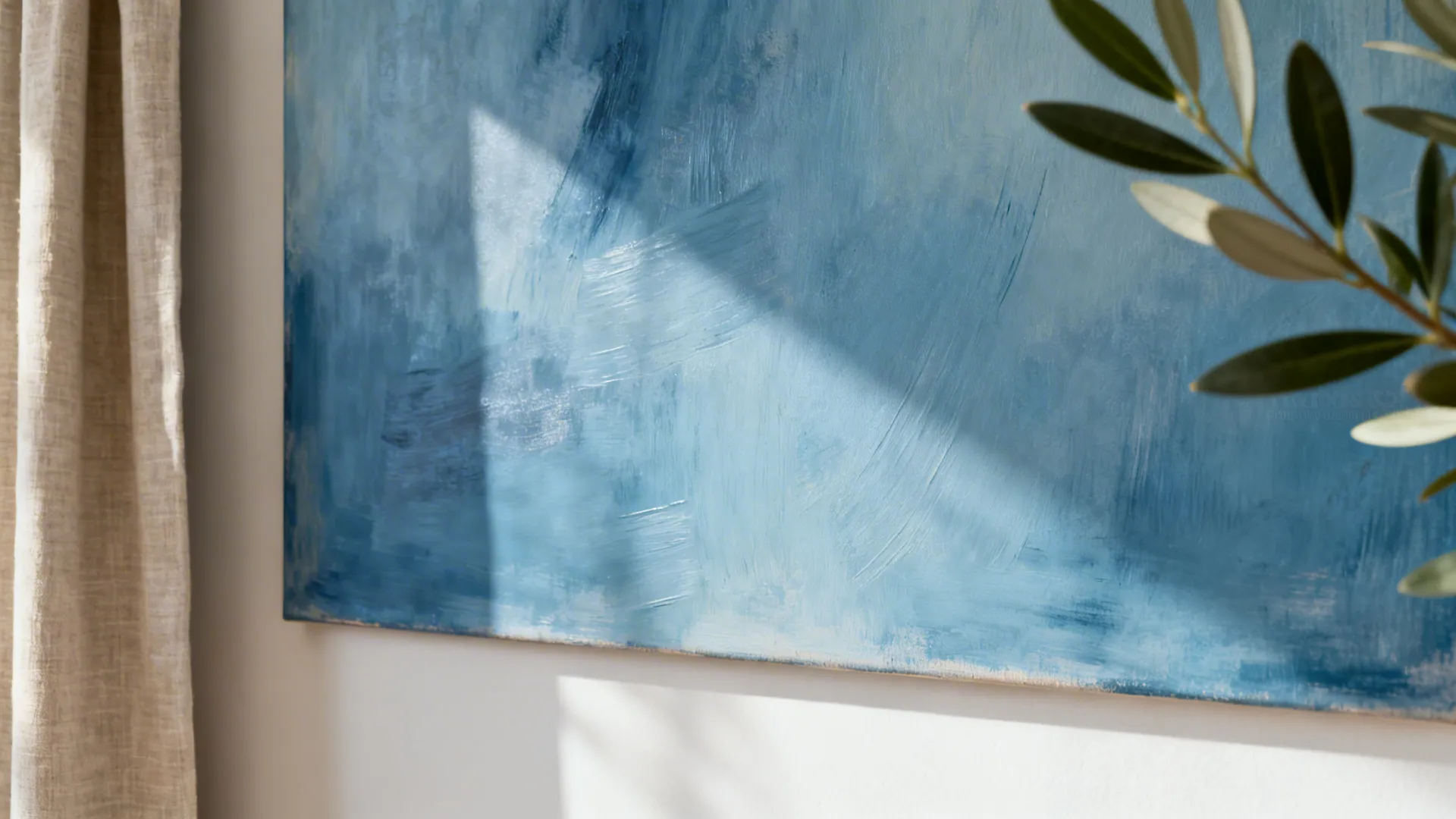 Macro detail of blue abstract art with linen and olive tree accents in a minimalist living room.