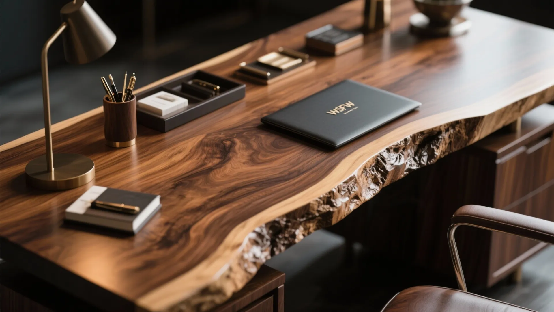 Close up of solid wood desk featuring natural live edge with brass lamp and office stationery