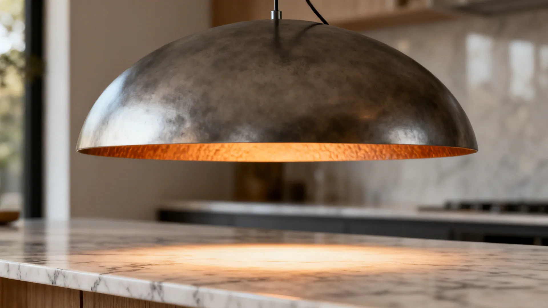 Close-up of a large sculptural pendant hung above a marble kitchen island, showing material and warm light
