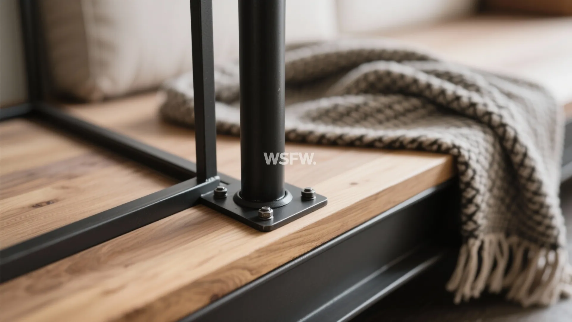 Close up of black metal bed frame bolted to wooden floor with a grey blanket