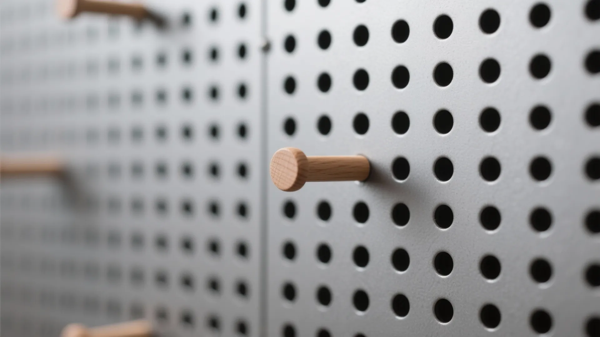 Macro of matte steel pegboard with a wood peg, showing hole pattern and satin finish.