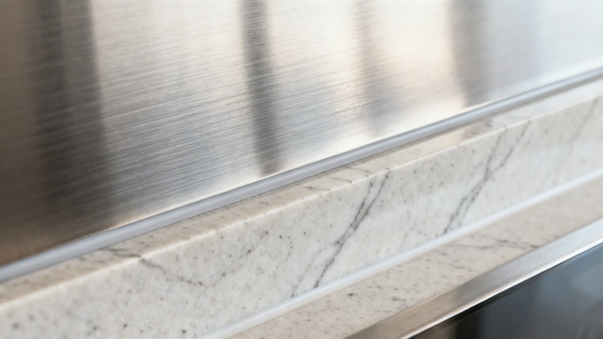Macro of brushed stainless grain next to a honed quartz run-up seam.