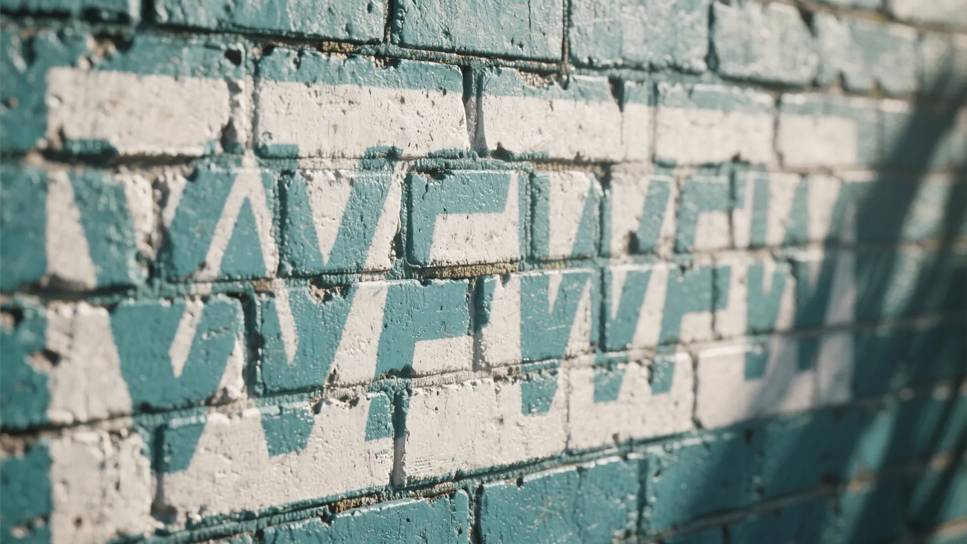 Close up of teal painted brick wall with white stencil patterns and soft natural shadows
