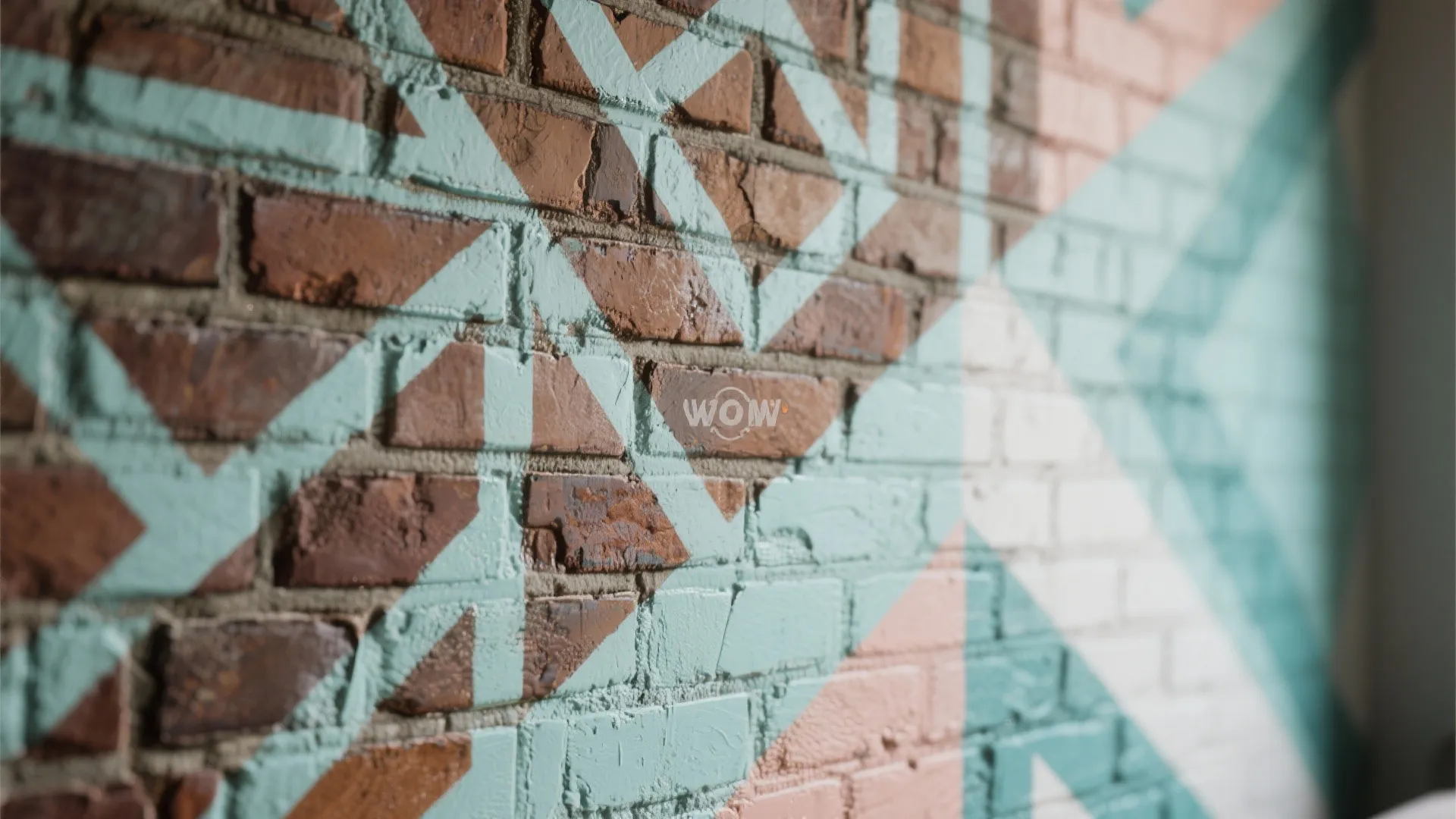 Close up of a brick wall featuring painted geometric patterns in light blue and pink colors