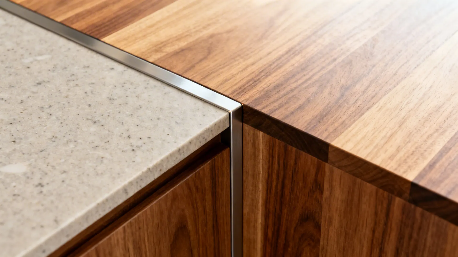 Close-up of a slim metal band separating quartz and butcher block on a stepped L-shaped island.