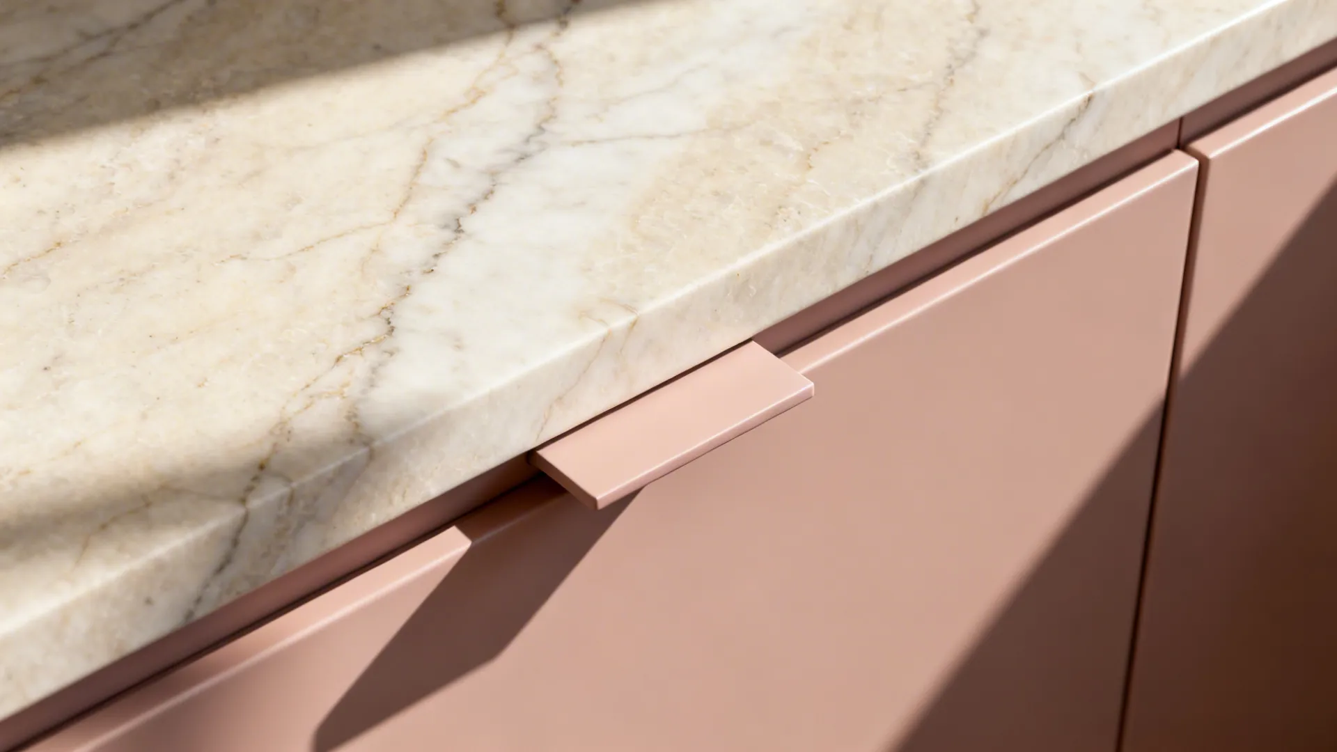 Macro of veined stone countertop meeting nude-pink matte cabinet with thin finger pull.