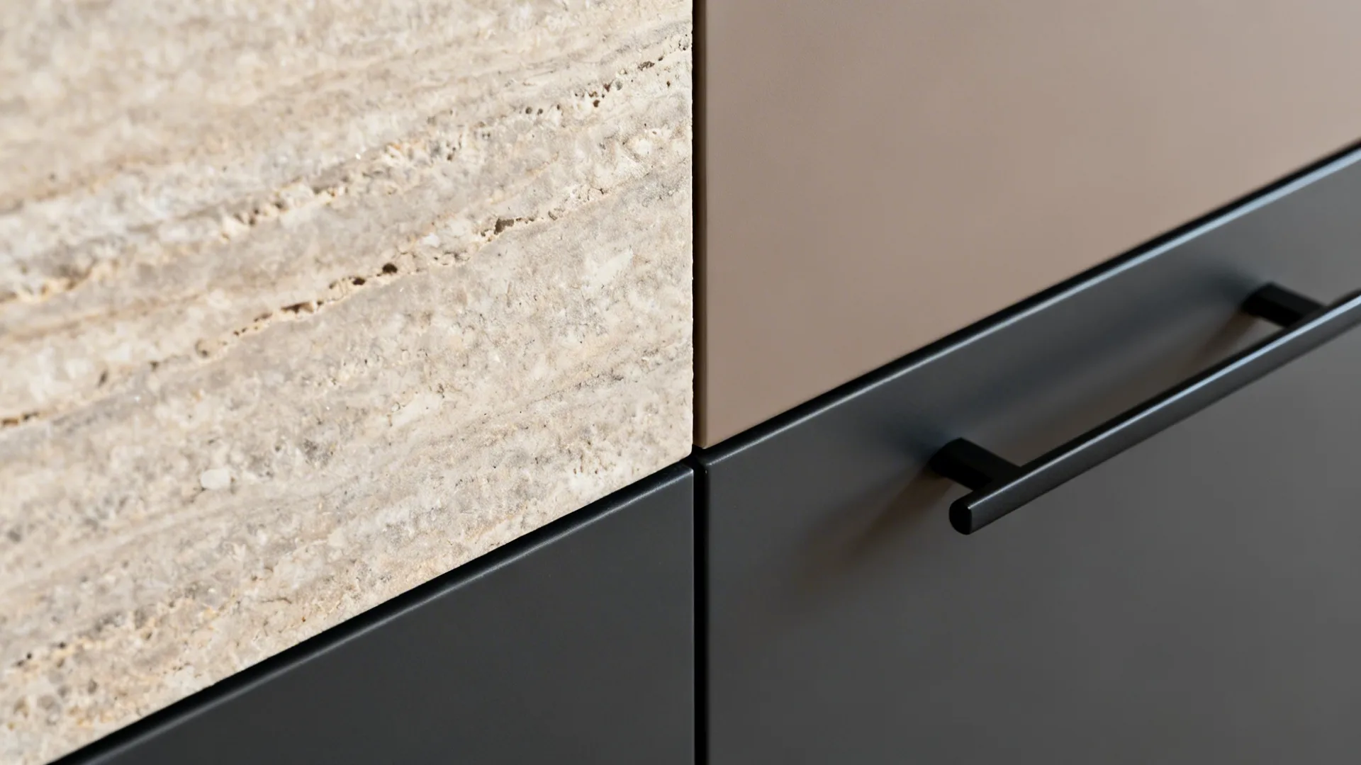 Macro of textured stone backsplash meeting charcoal and taupe cabinetry with slim black pull.