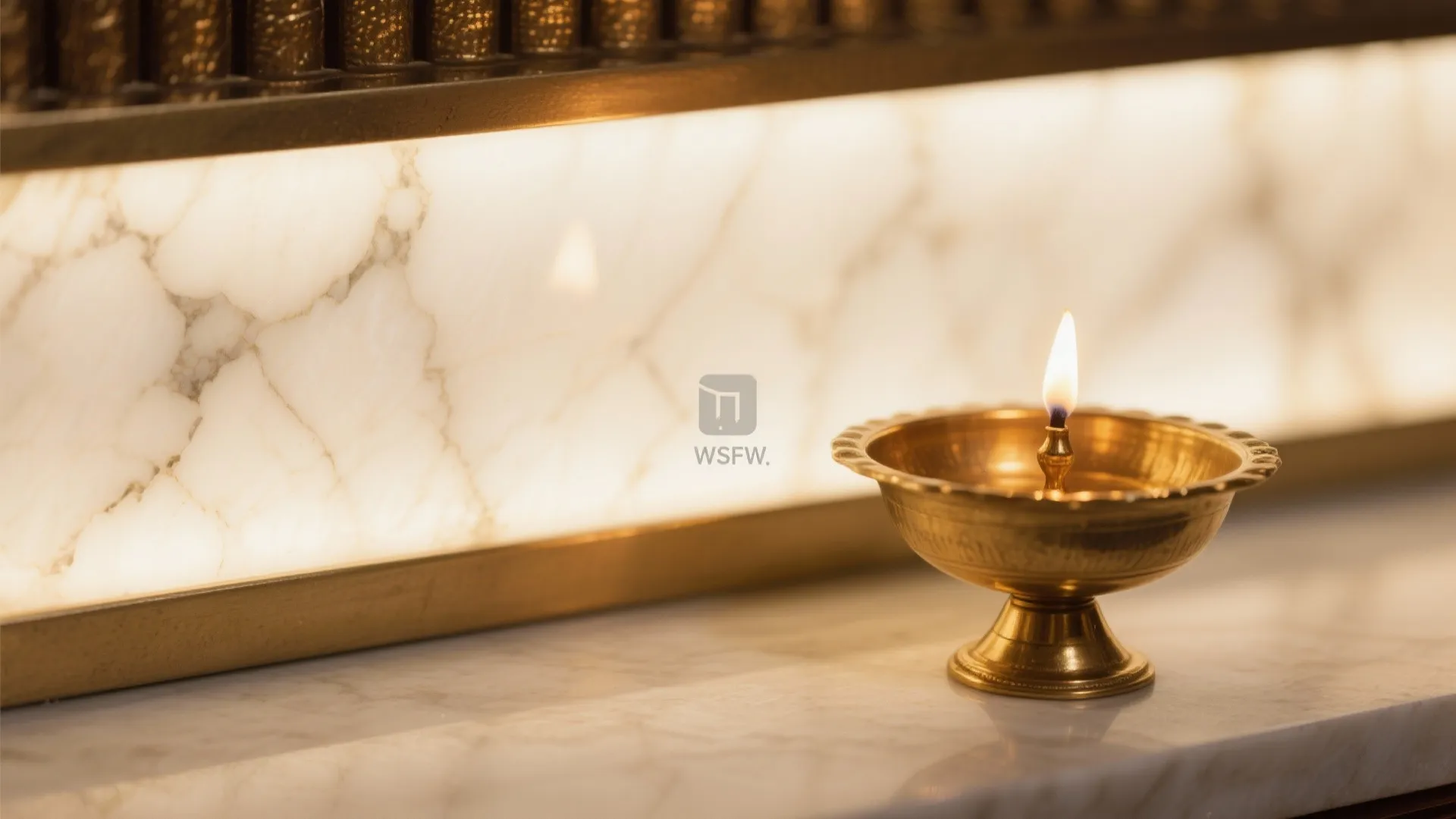 Close up of a small gold oil lamp burning on a white marble table surface