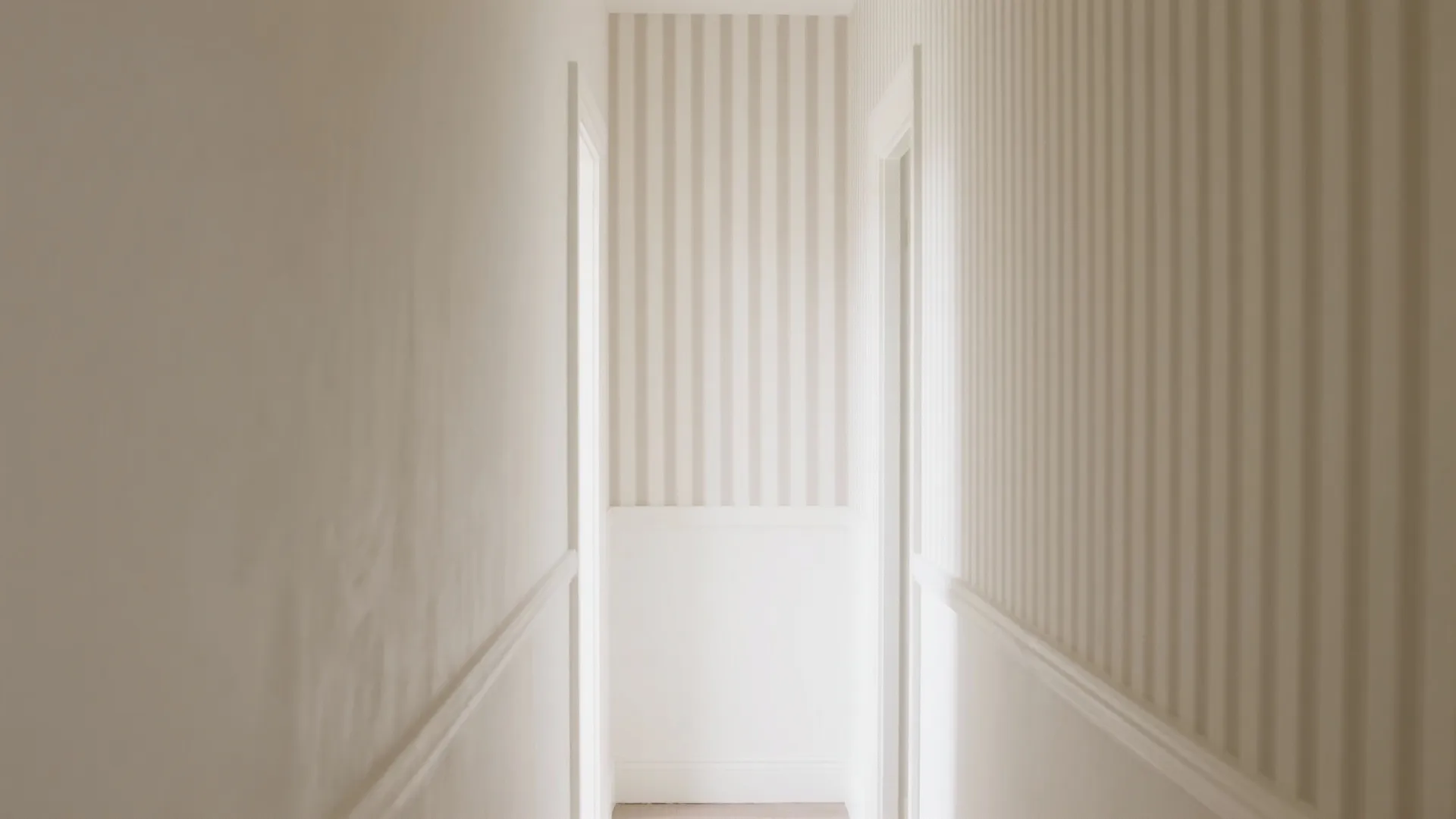 Narrow hallway with vertical striped wallpaper above warm-white paint, creating an illusion of height.