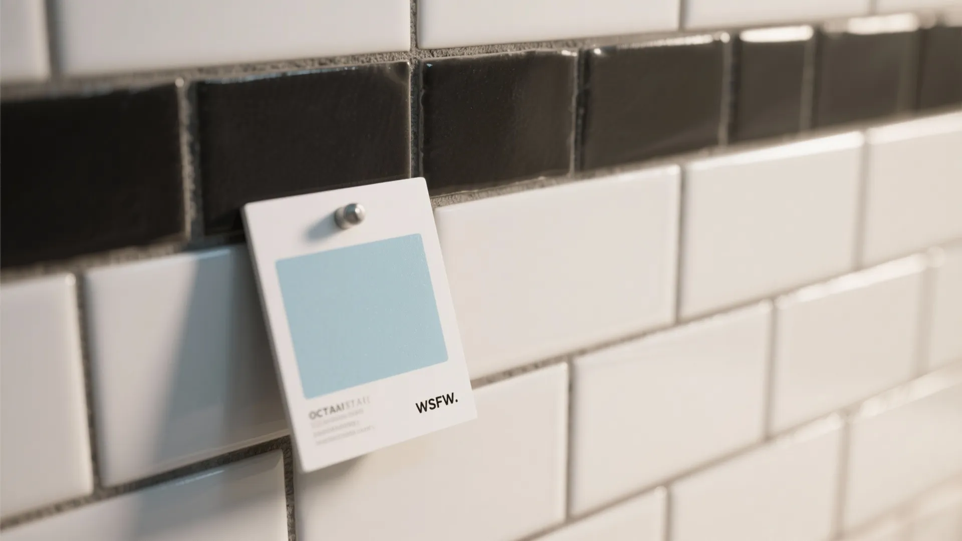 Close up of white subway wall tiles featuring a black grout line and blue sample