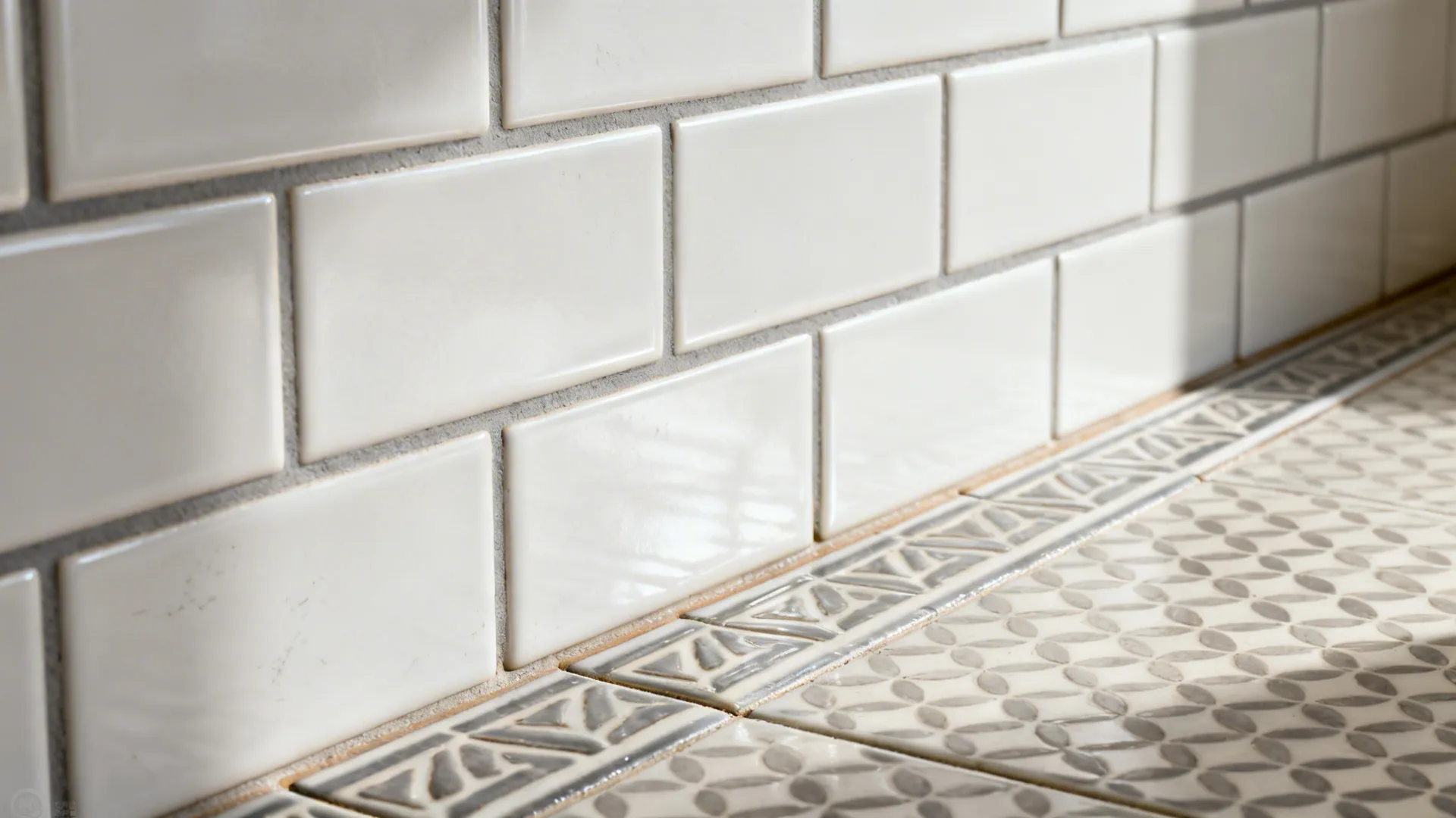 Macro of matte white subway tile with soft gray grout beside patterned porcelain floor.