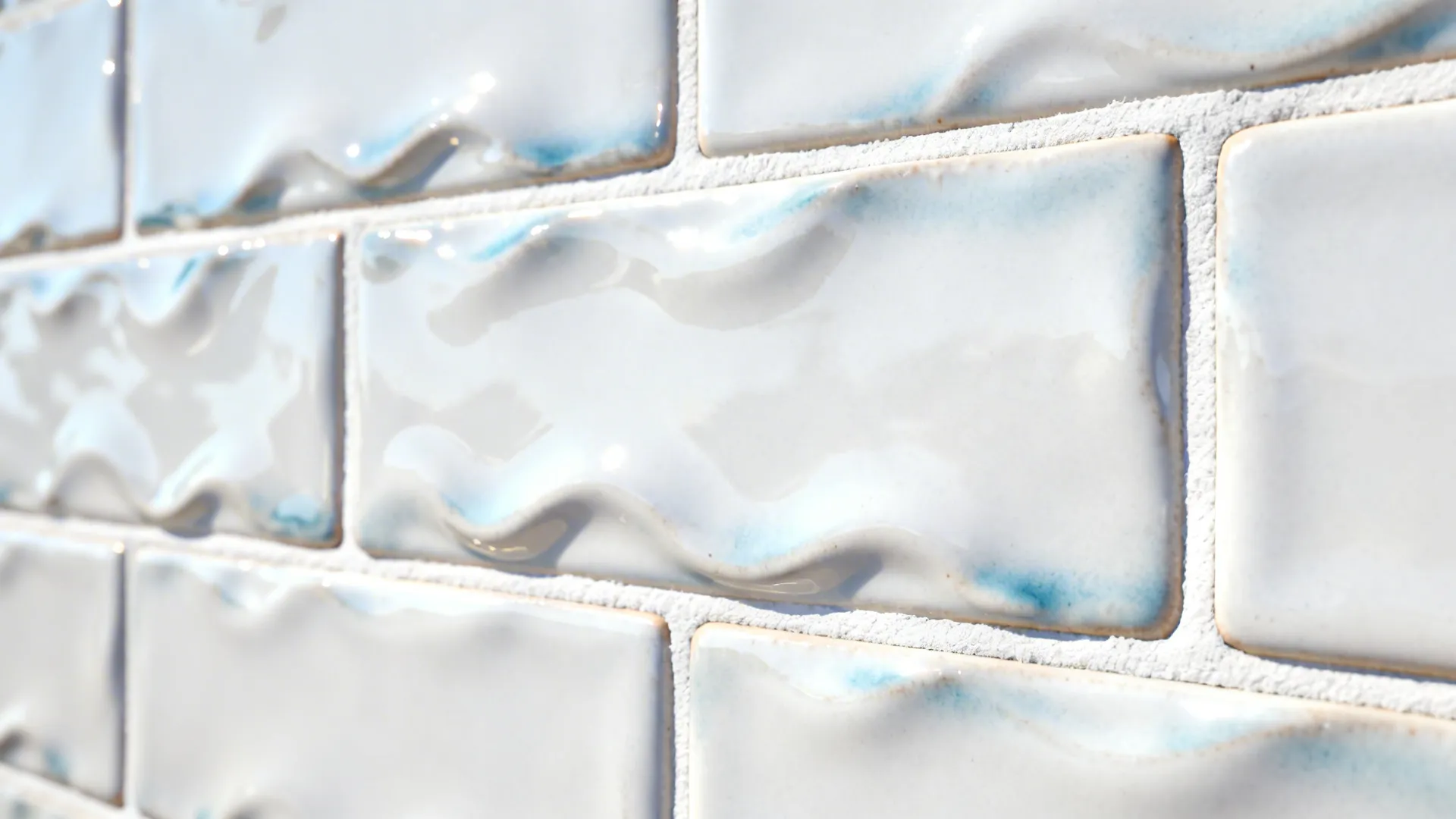 Macro of wavy handmade-look white subway tile with off-white epoxy grout.
