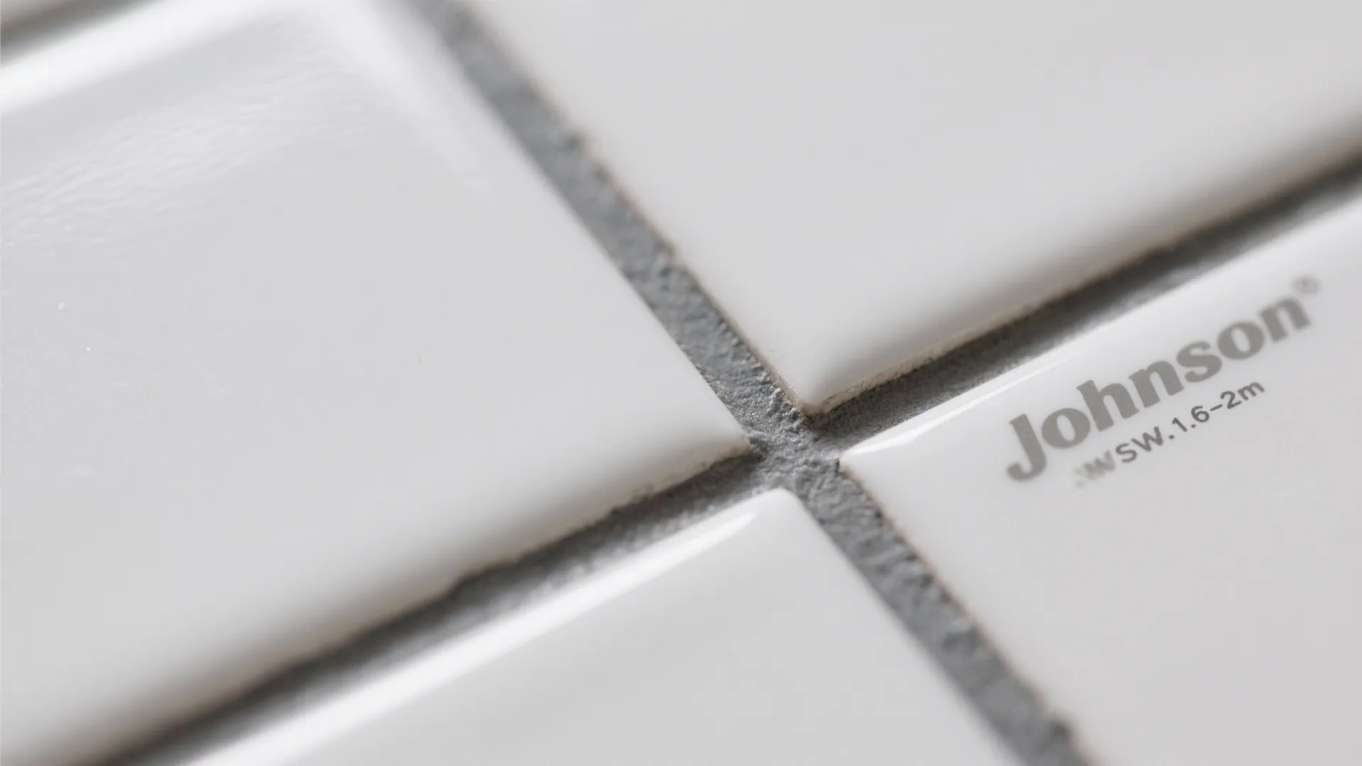 Close up of white wall tiles with grey grout showing brand name and small printed text