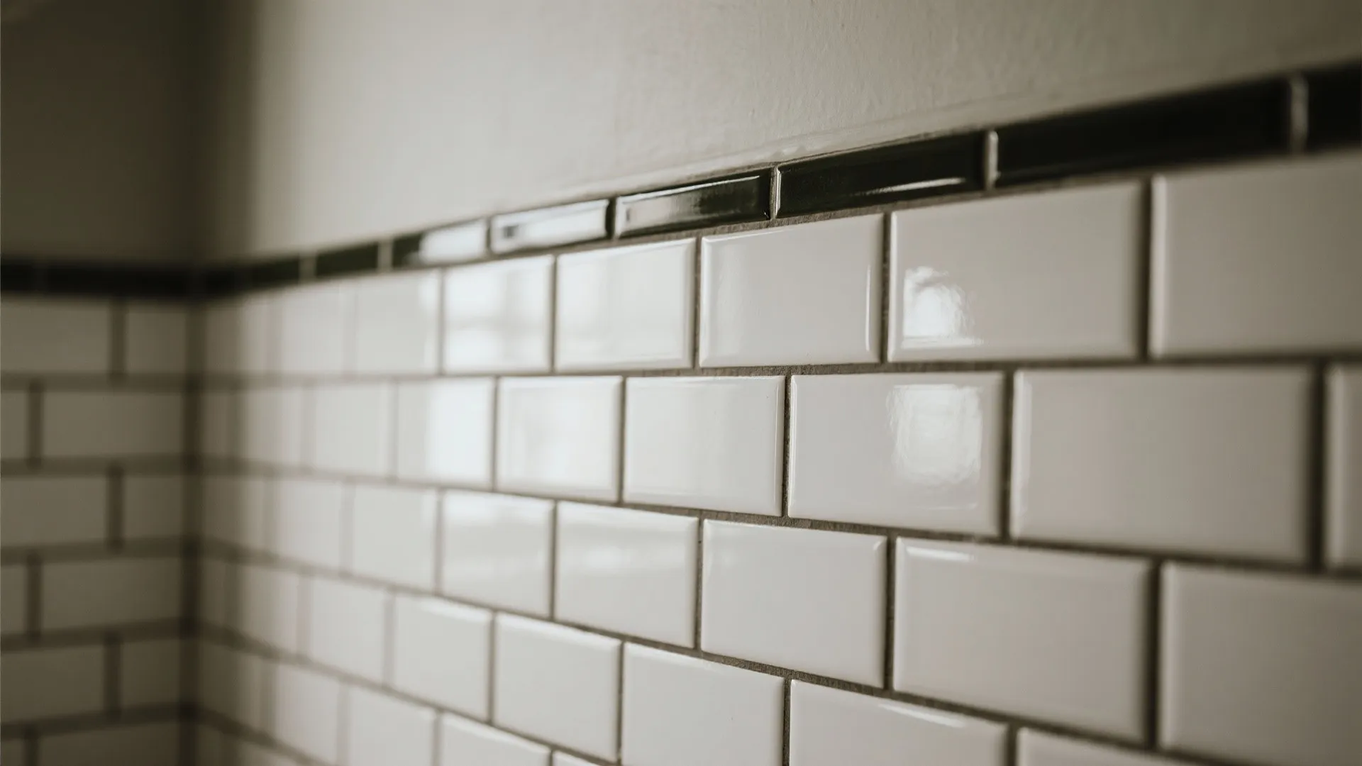 Close up of white wall tiles with dark grout and a black border on top