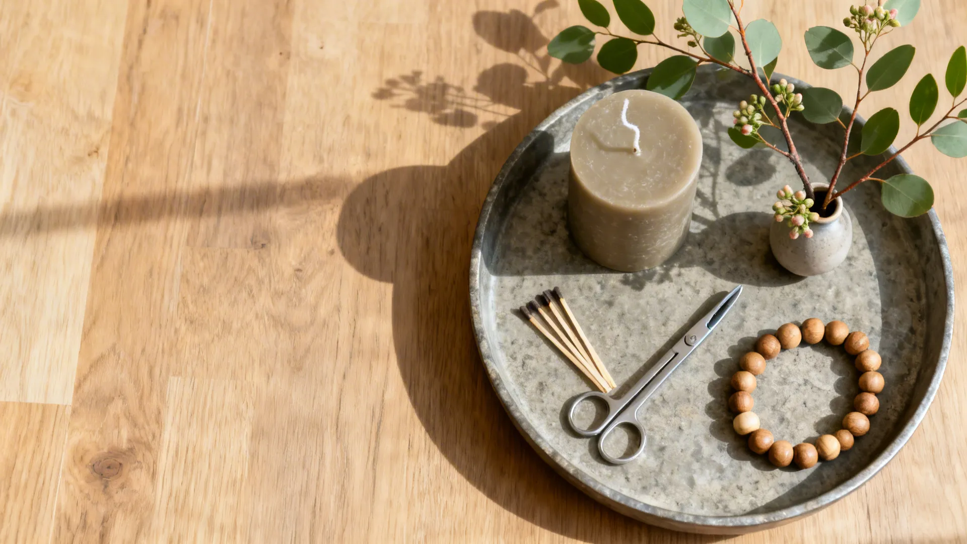 Top-down flat lay of a tray, neutral candle, wick trimmer, beads, branch, and bud vase.
